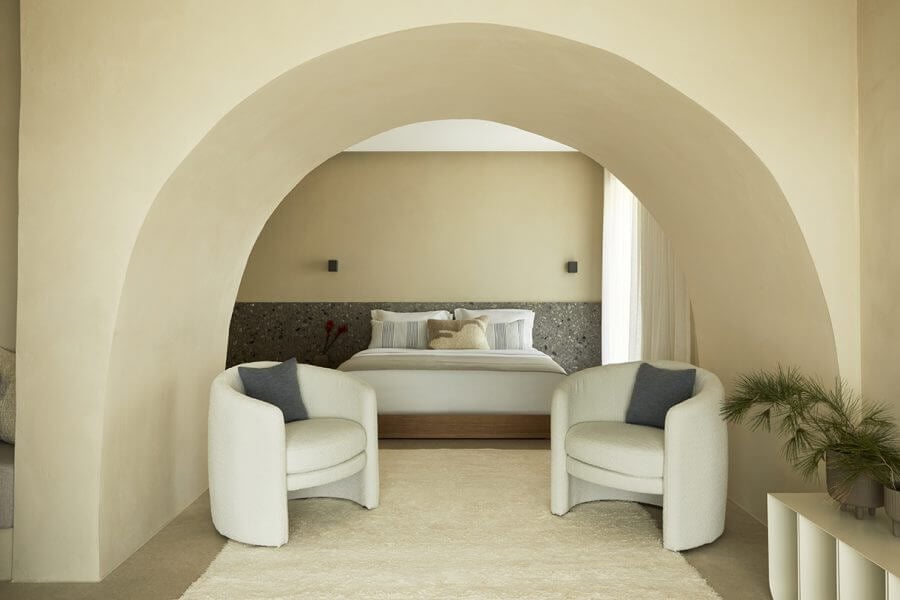 Pārocks, Europe — Minimalist bedroom suite with curved archway, cream walls, rounded armchairs, and textured headboard wall.