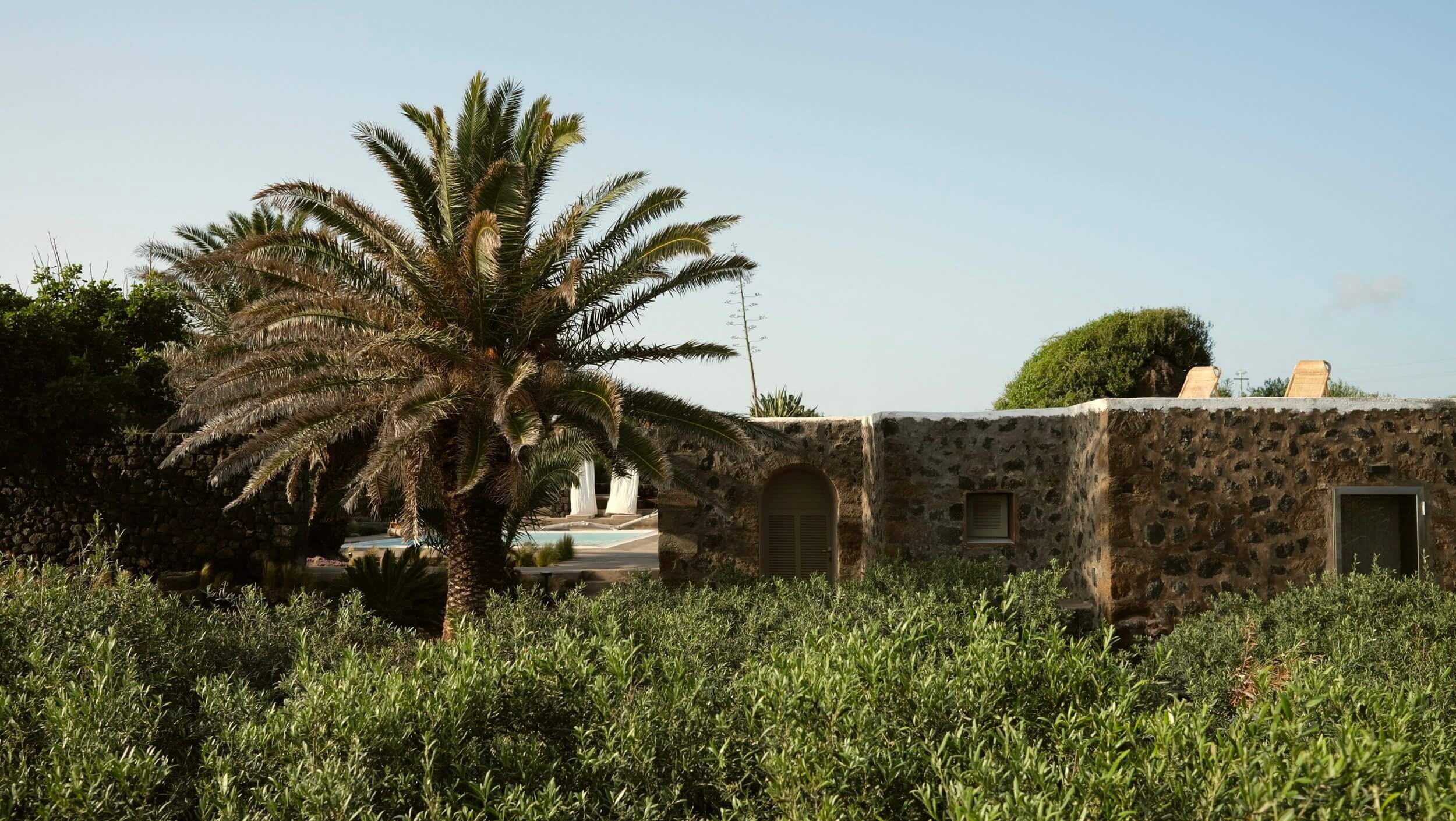 Parco Dei Sesi, Europe — Stone villa with arched entrance surrounded by olive trees and palm, clear sky, Mediterranean landscape aesthetic.