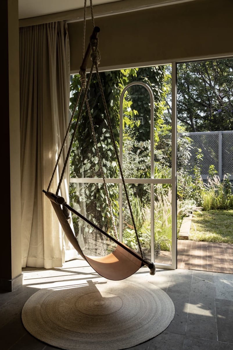 UMA Casa, Mexico — Suspended leather swing with rope hanging in minimalist room overlooking lush garden through floor-to-ceiling glass doors, natural light casting shadows on concrete floor with woven rug.