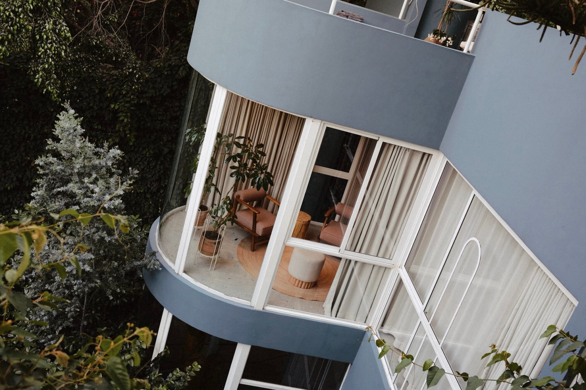 UMA Casa, Mexico — Curved modernist residence with floor-to-ceiling windows, terracotta furniture, linen curtains, and surrounding native vegetation under bright daylight.