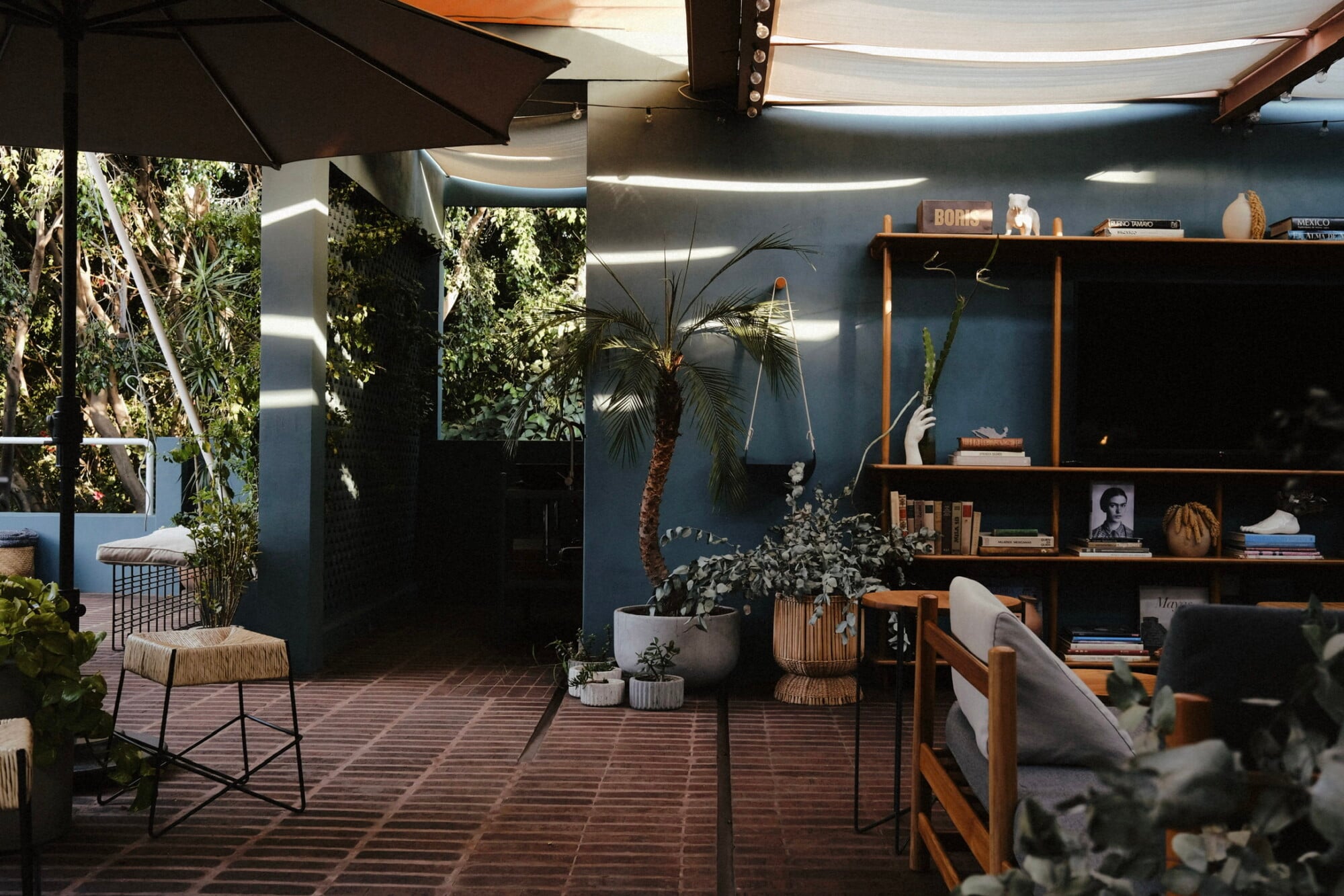 UMA Casa, Mexico — Dark teal interior with wooden shelving, potted palms, woven seating, geometric tile flooring, and retractable shade structures creating sophisticated resort ambiance.