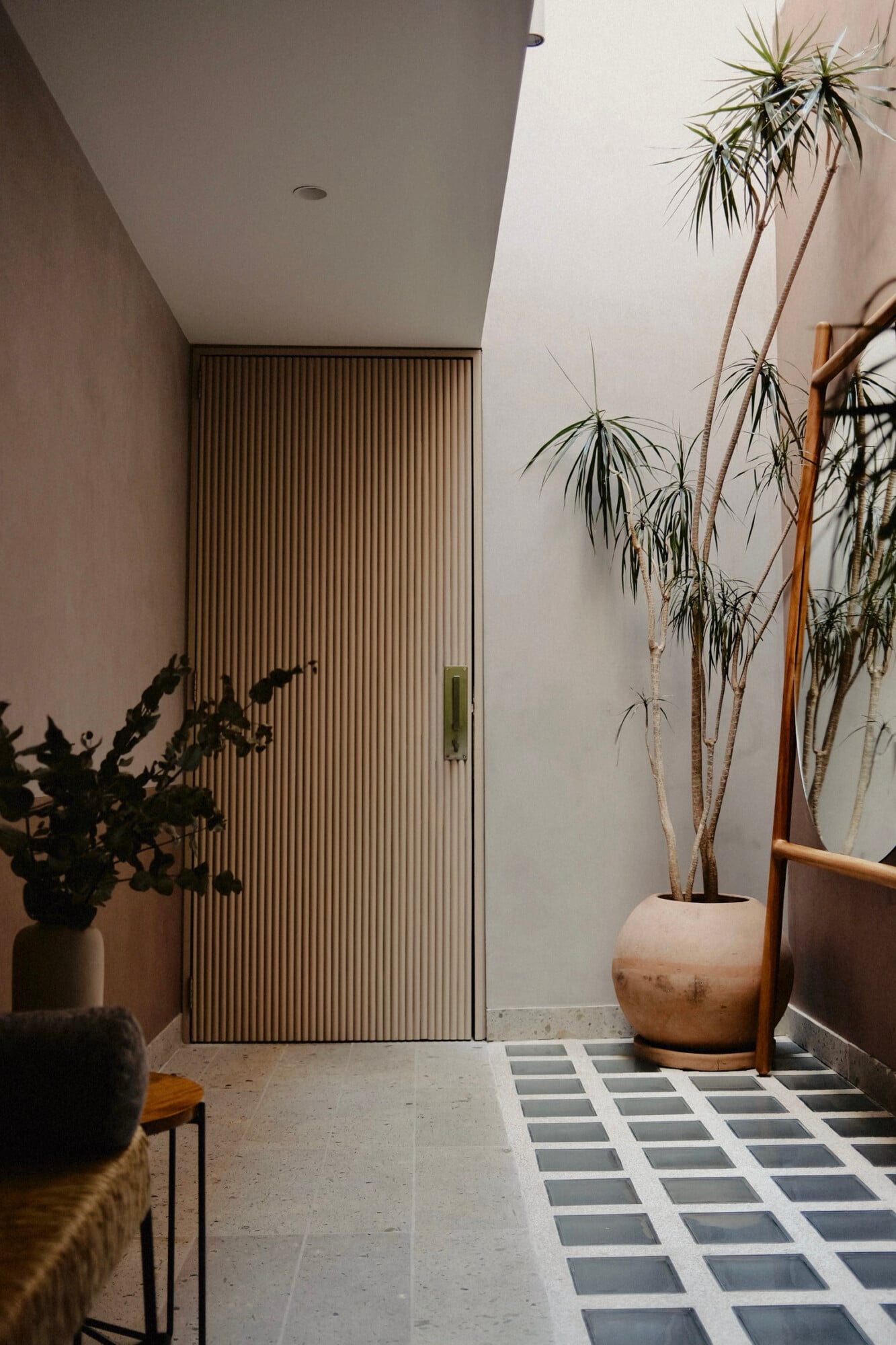 UMA Casa, Mexico — Minimalist entryway with vertical ribbed door, concrete flooring, potted palms, and geometric tile pattern in natural light.