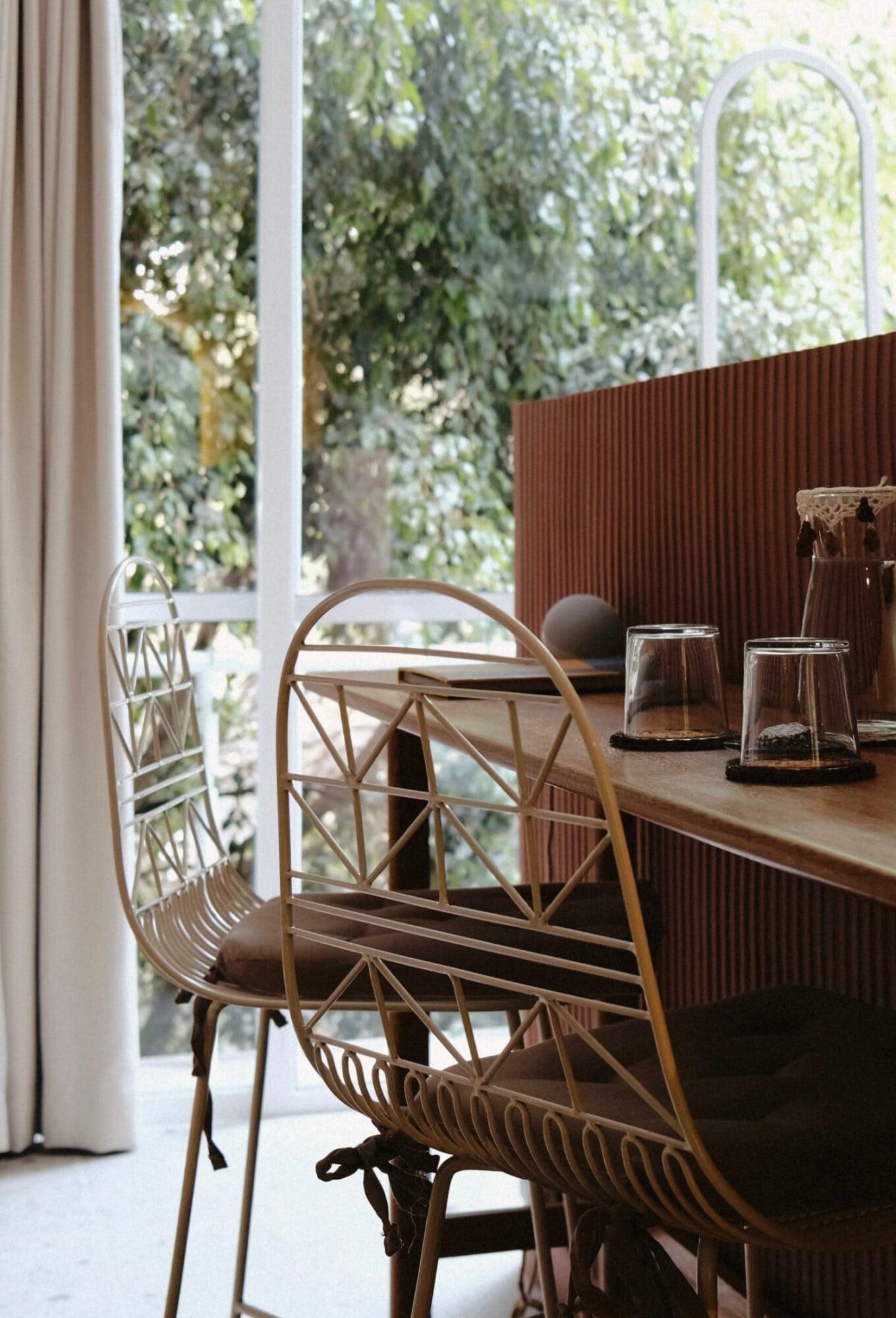 UMA Casa, Mexico — Rattan chair at timber desk beside floor-to-ceiling windows overlooking verdant garden, natural light filtering through sheer curtains.