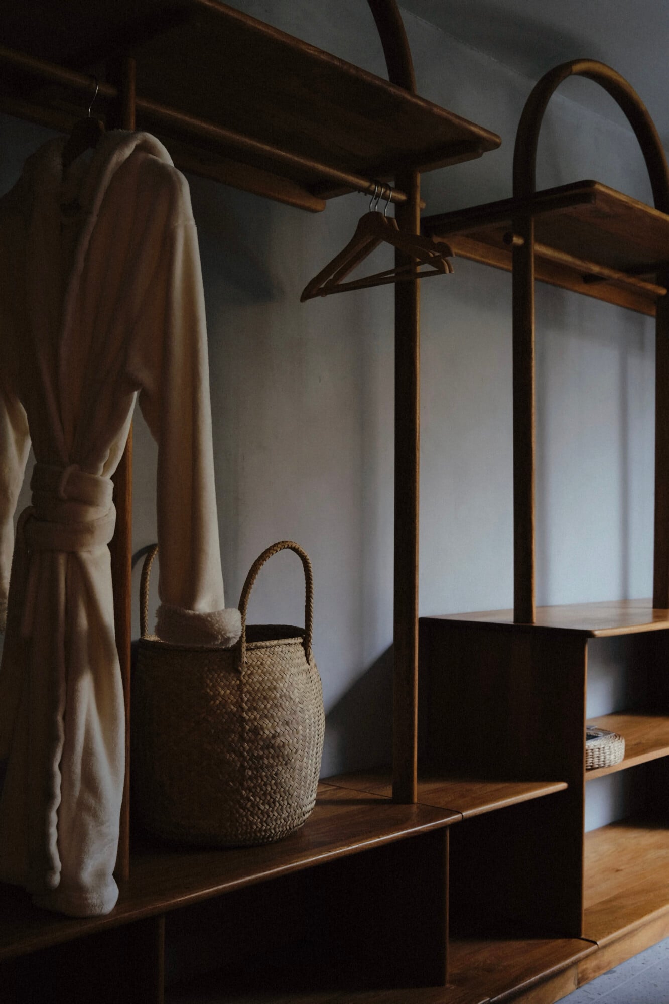 UMA Casa, Mexico — Wooden shelving with woven basket, cream linen, and wooden hanger casting shadows on whitewashed wall, minimalist hospitality design.
