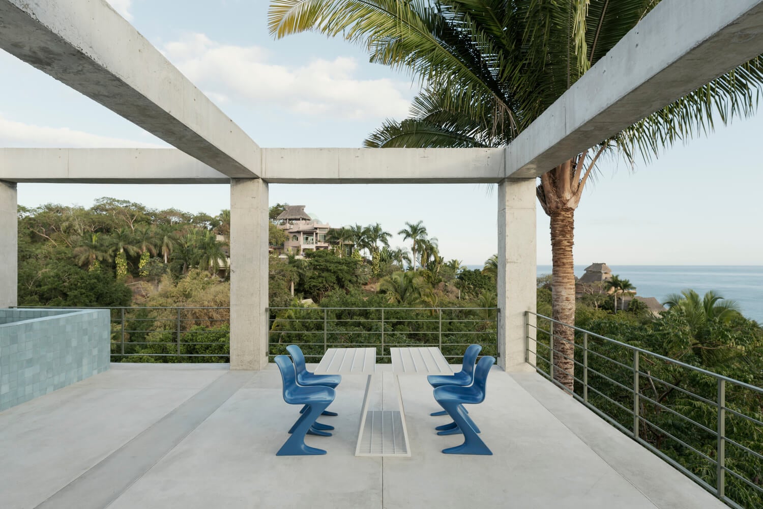 NICO, Mexico — Concrete terrace with blue sculptural chairs overlooking palm-lined hillside and ocean vista, minimalist architectural design.