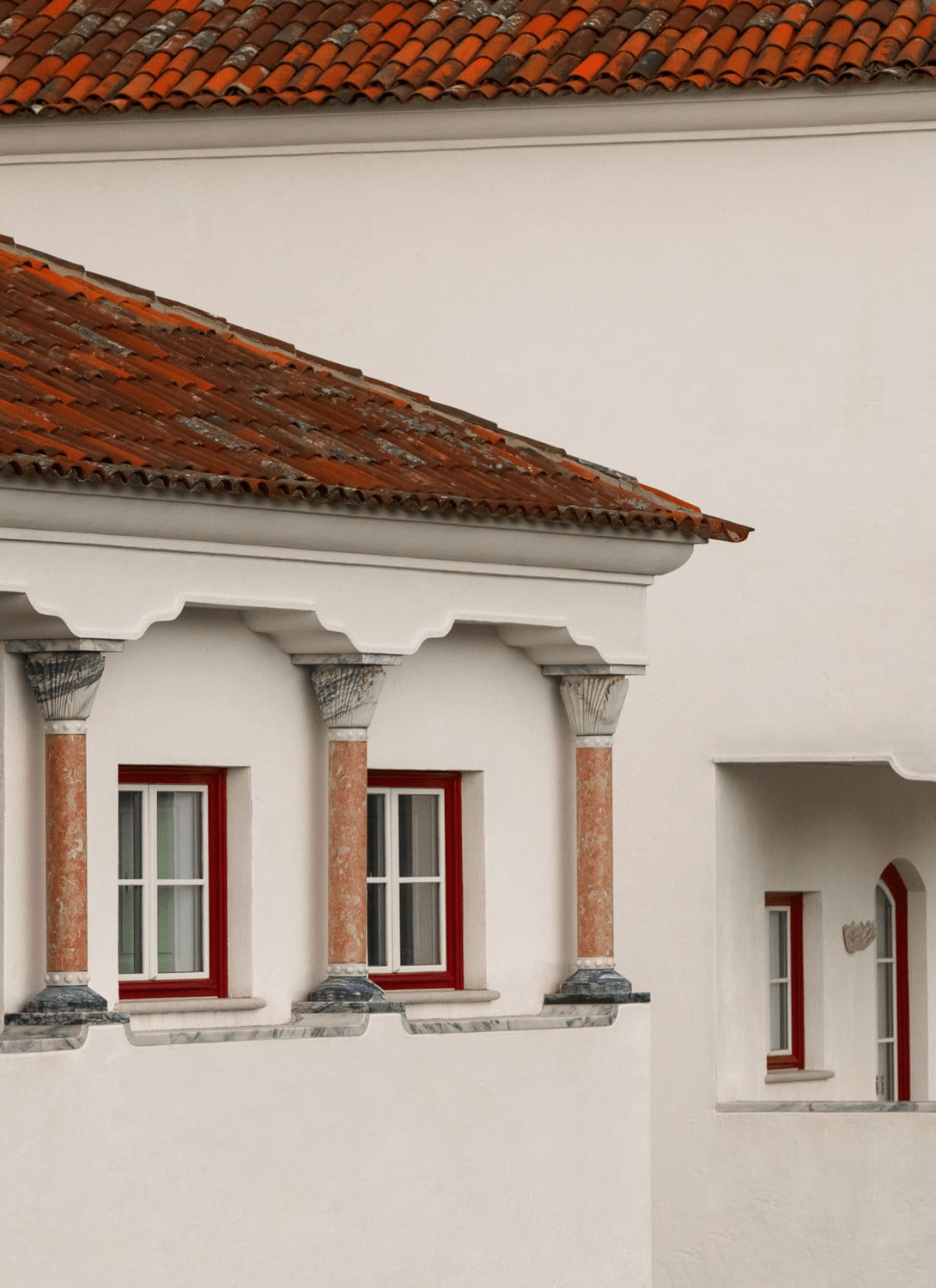 Vermelho, Europe — Whitewashed colonial facade with terracotta tile roof, ornate columns, red-trimmed windows, and weathered wooden eave detail.