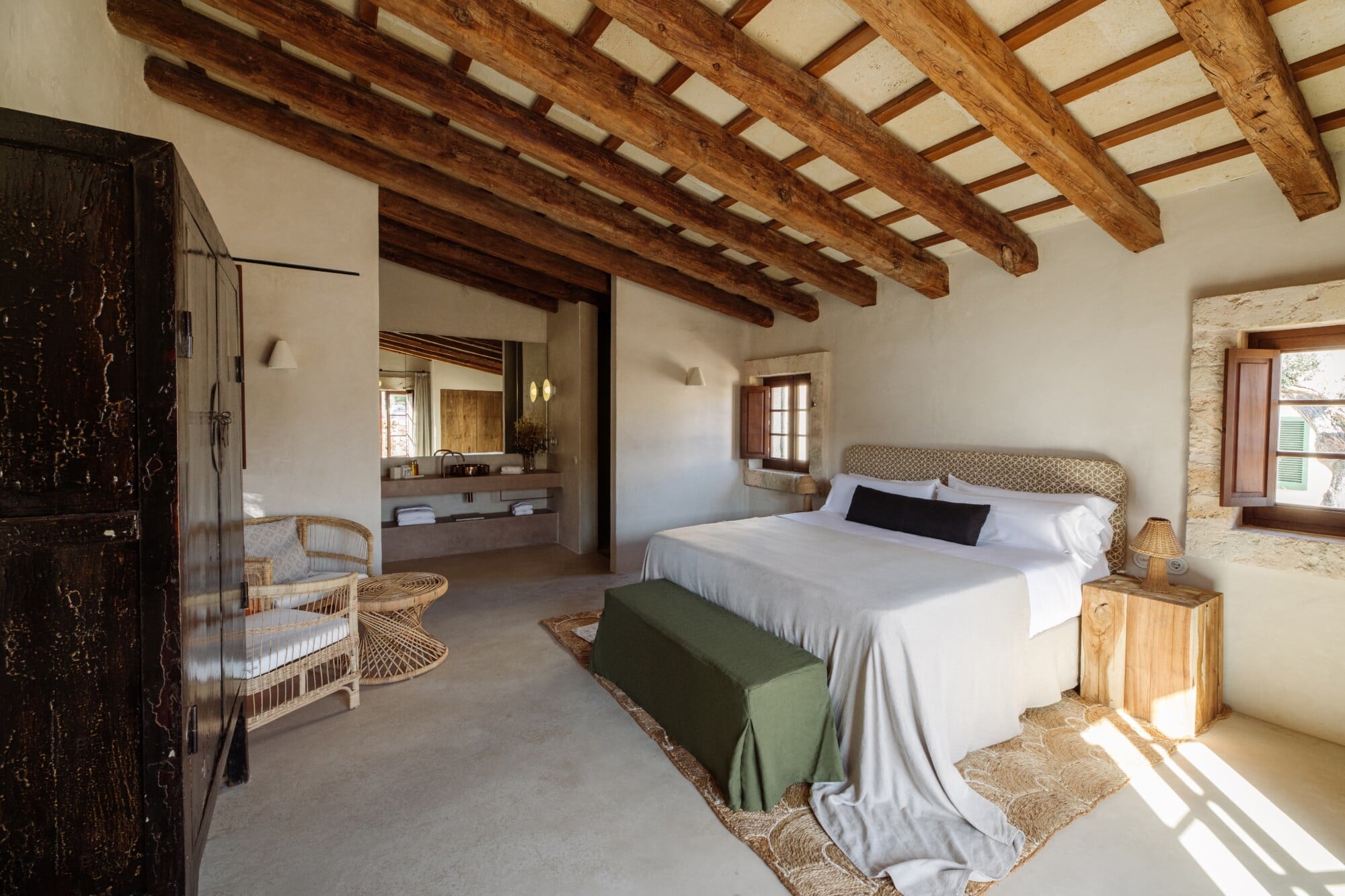 Santa Ana, Balearic Islands — Spacious bedroom with exposed wooden beams, stone walls, wicker furnishings, and natural light from multiple windows.