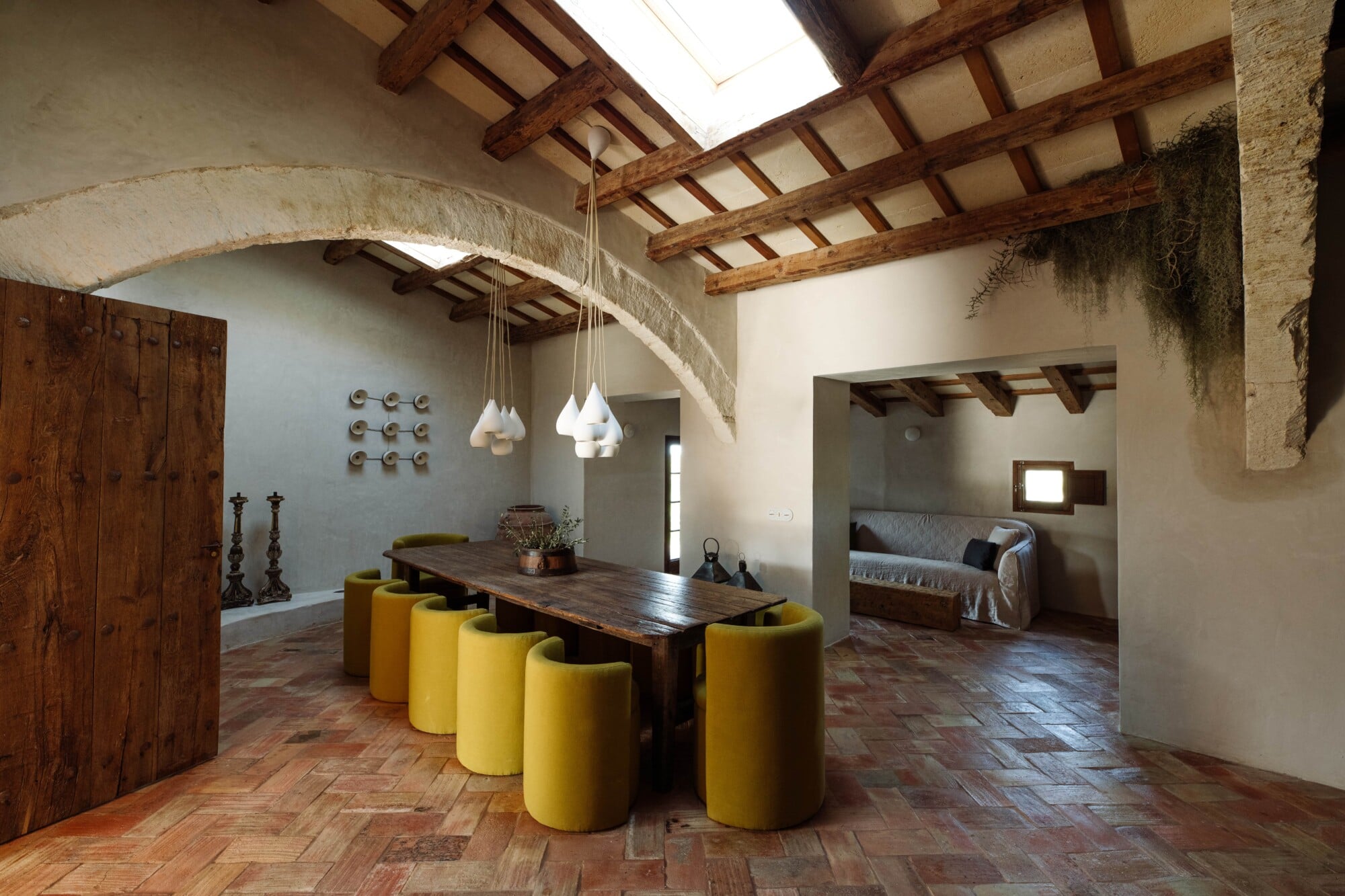 Santa Ana, Balearic Islands — Dining room with exposed wooden beams, arched stone ceiling, yellow cylindrical seating, dark wood table, pendant lights, terracotta flooring.