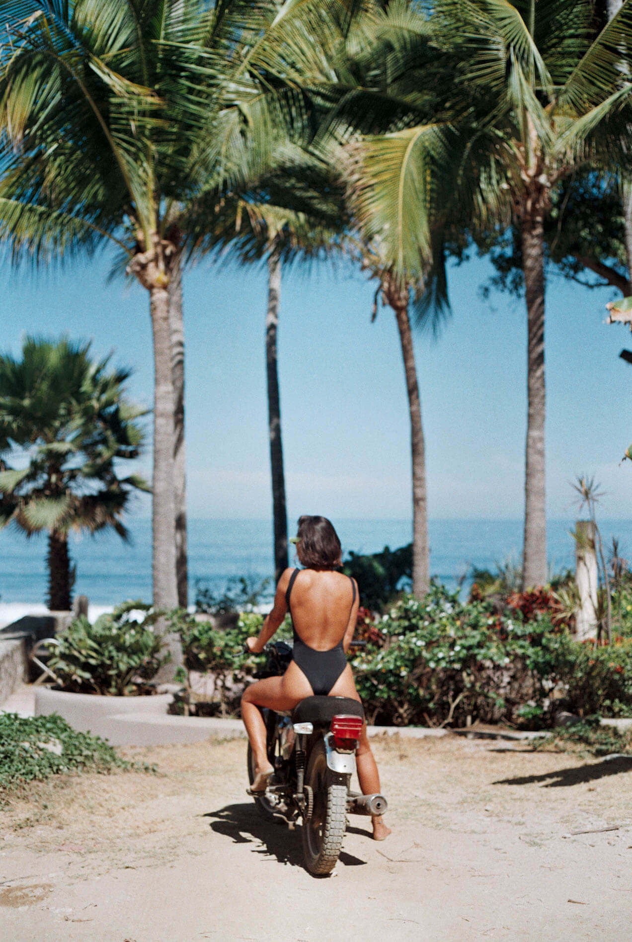 Sayulita Beach, Mexico — Person riding vintage bicycle through palm-lined sandy path toward ocean under clear blue sky, tropical coastal aesthetic.