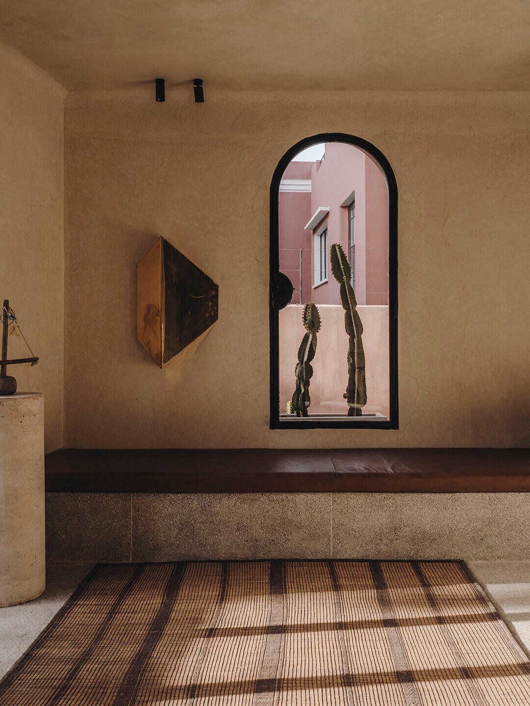 Maison Brummell Majorelle, Africa — Minimalist interior with arched window framing cacti, terracotta walls, geometric tile floor, and modernist wall art in warm earth tones.
