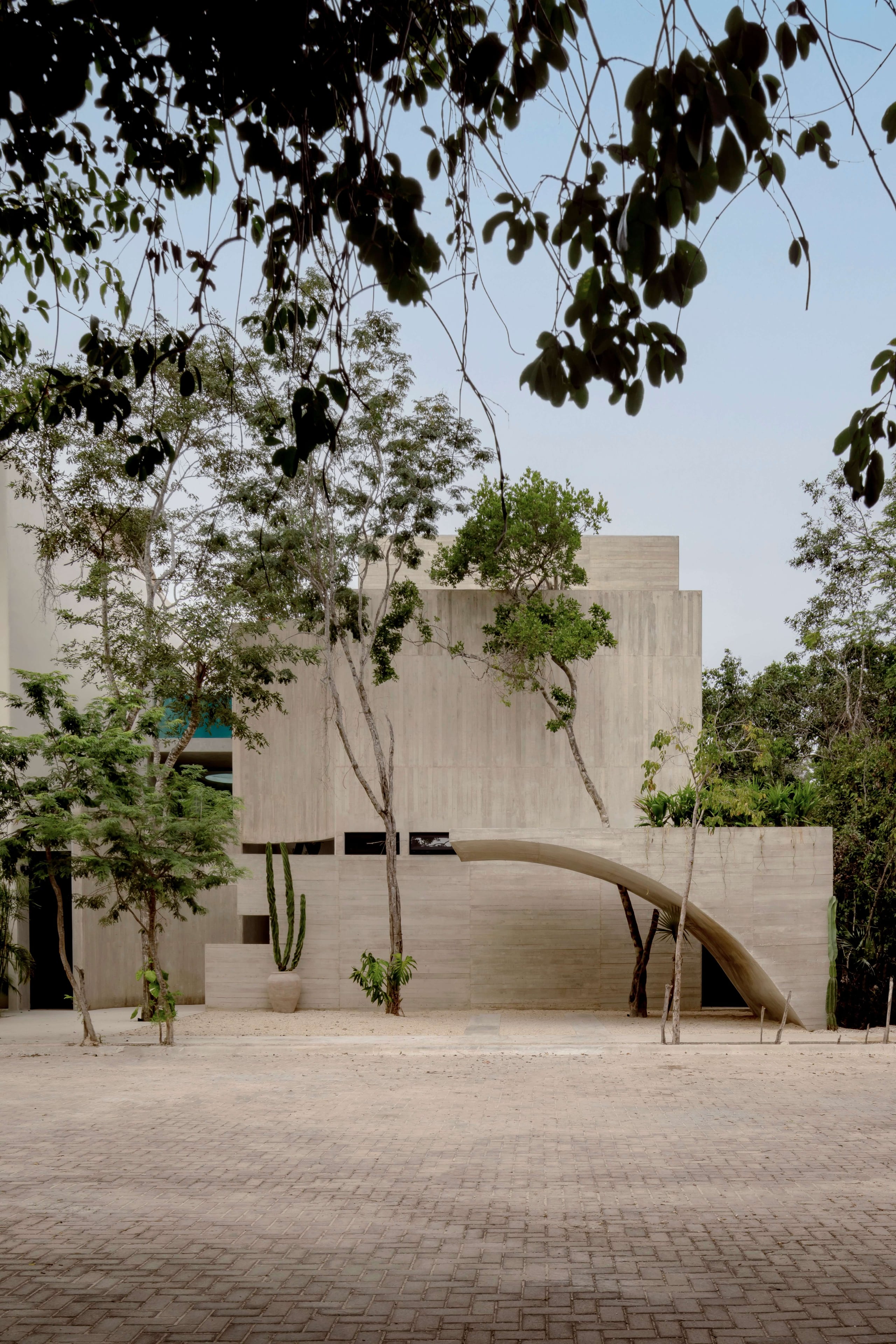 Villa Cava, Mexico — Minimalist concrete residence with curved archway, native trees, and geometric facade in desert courtyard setting.