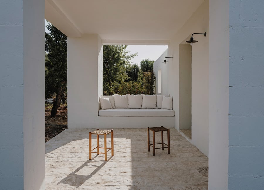 Masseria Moroseta, Europe — Covered terrace with built-in daybed, wooden stools, and black showerheads overlooking olive trees and gardens.