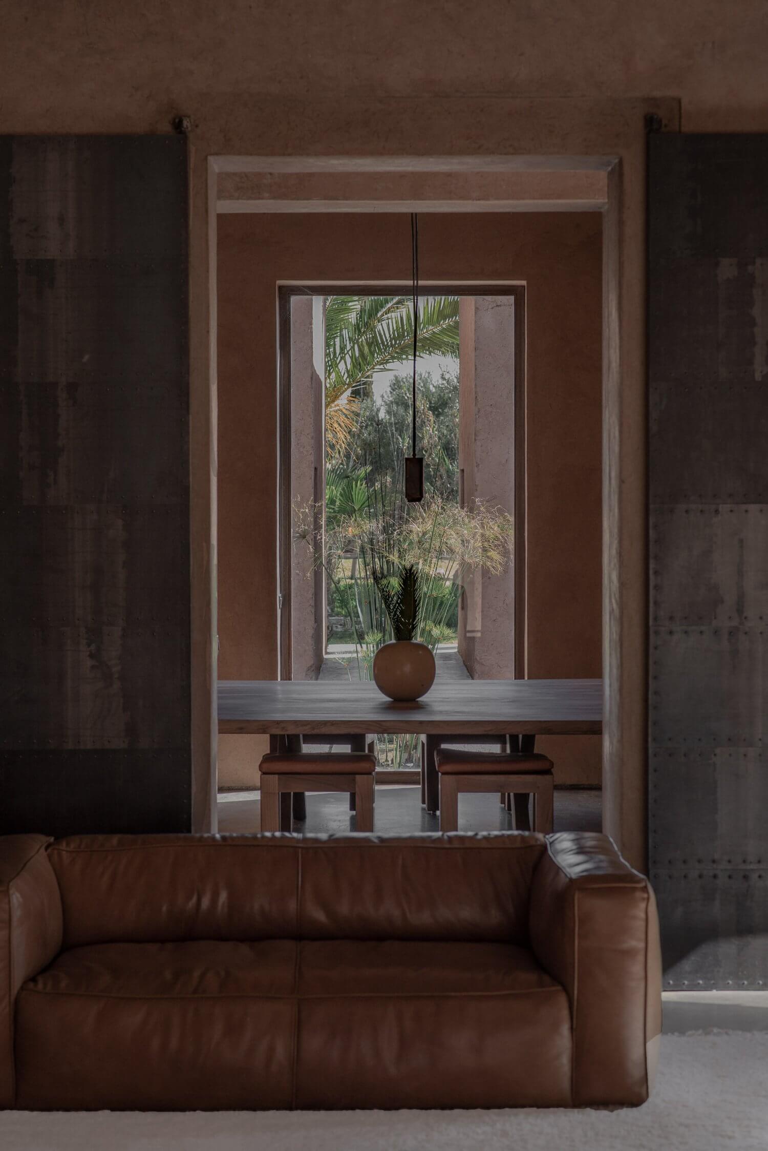 Villa D, Africa — Minimalist interior with cognac leather sofa, glass doors opening to lush tropical garden, terracotta sphere on console table, warm earthy tones.