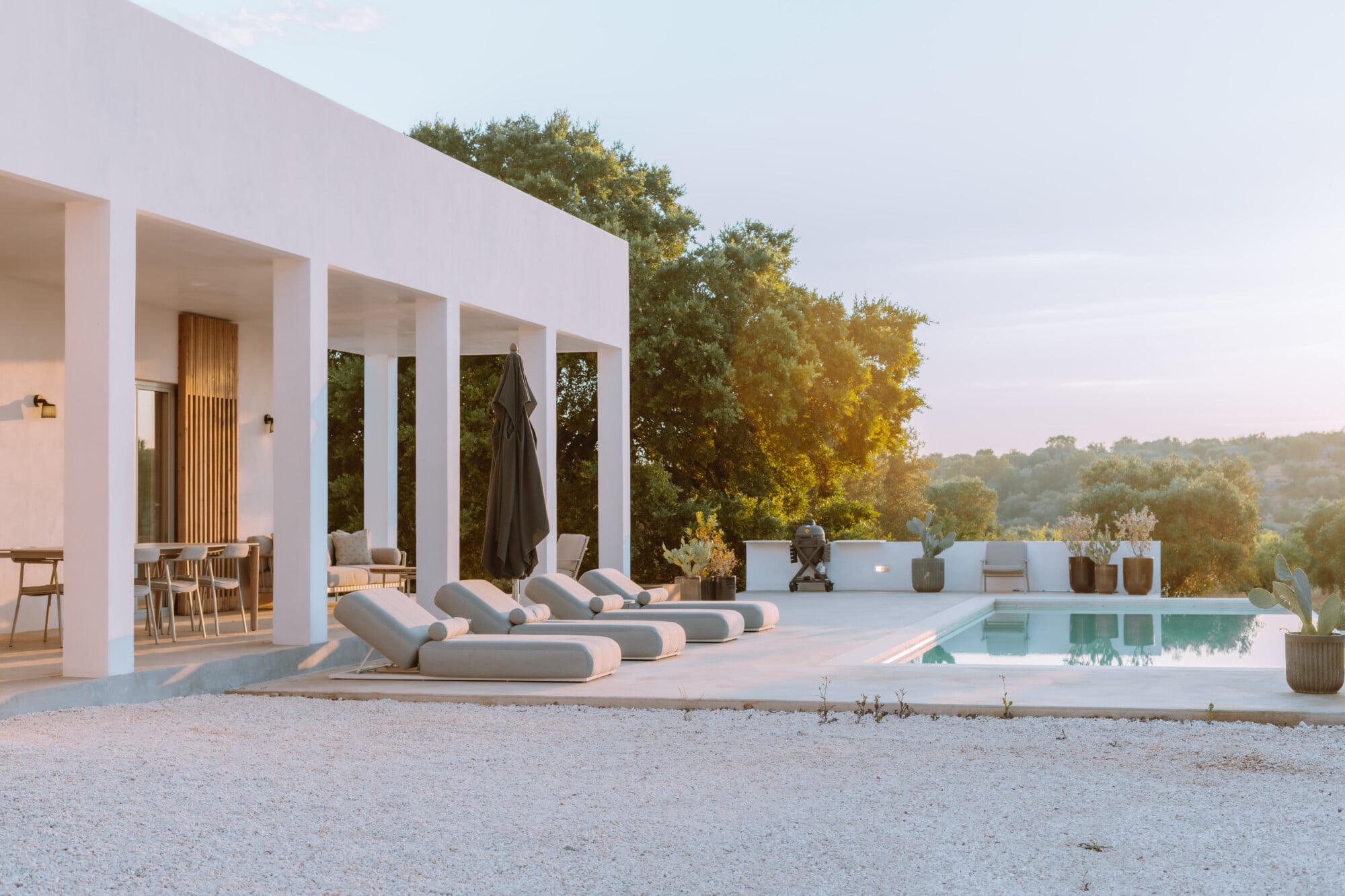 Villa Quercia, Italy — Modernist white villa with columned portico, terracotta pool deck, loungers, and forested hillside views at golden hour.
