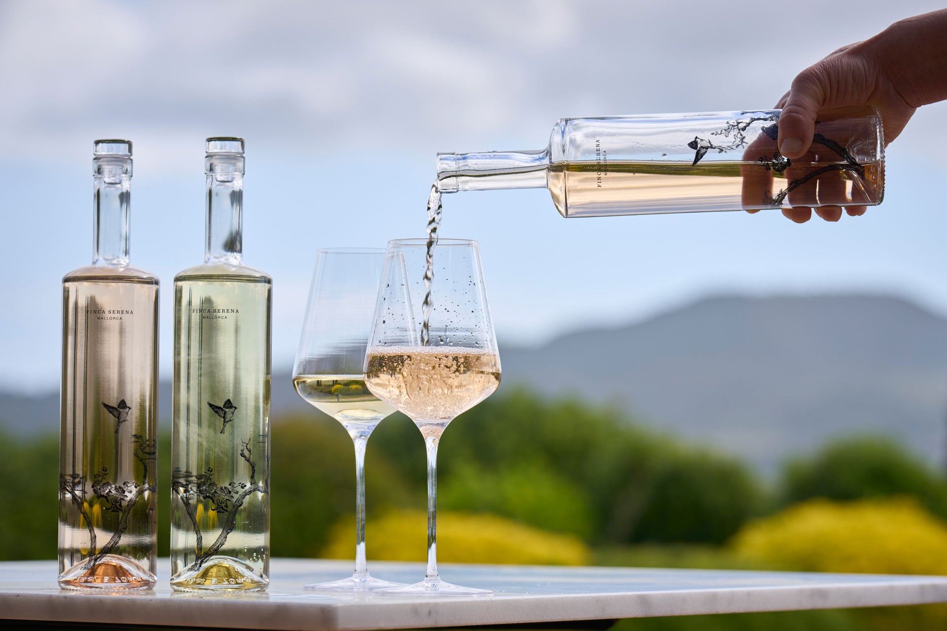 Finca Serena, Balearic Islands — White wine pouring into glasses with countryside vineyard views and Mediterranean landscape in soft daylight.
