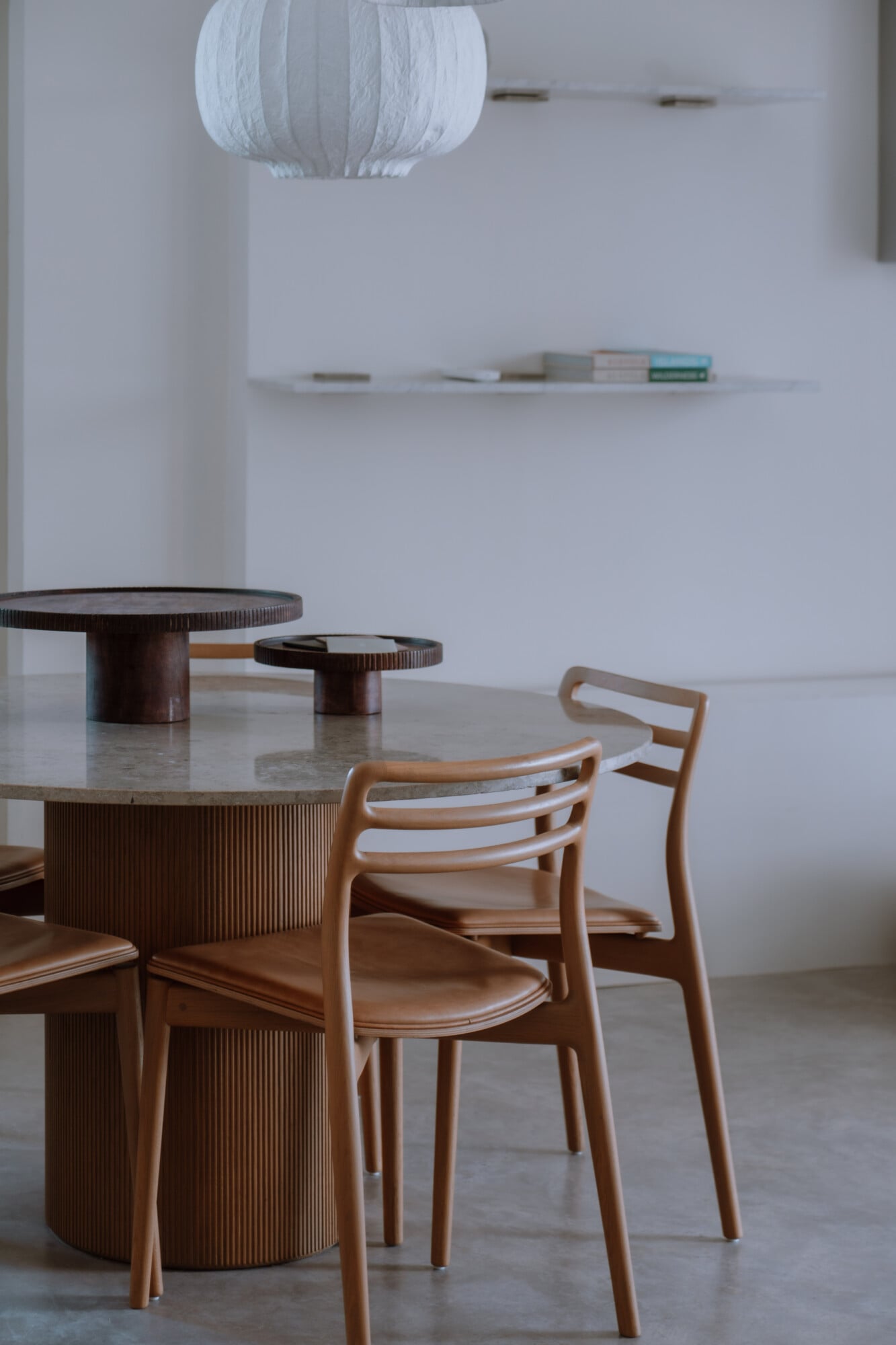 Villa Quercia, Italy — Minimalist dining room with fluted wood pedestal table, curved wooden chairs, stone countertop, and white paper pendant light.