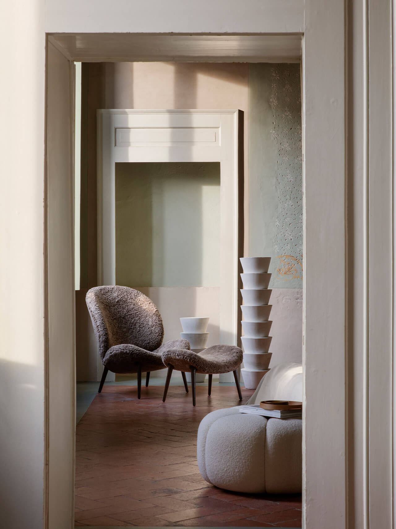 Vipp Palazzo Monti, Italy — Minimalist lounge with textured cream chair, curved ottoman, stacked white vessels, and natural light through open doorway.