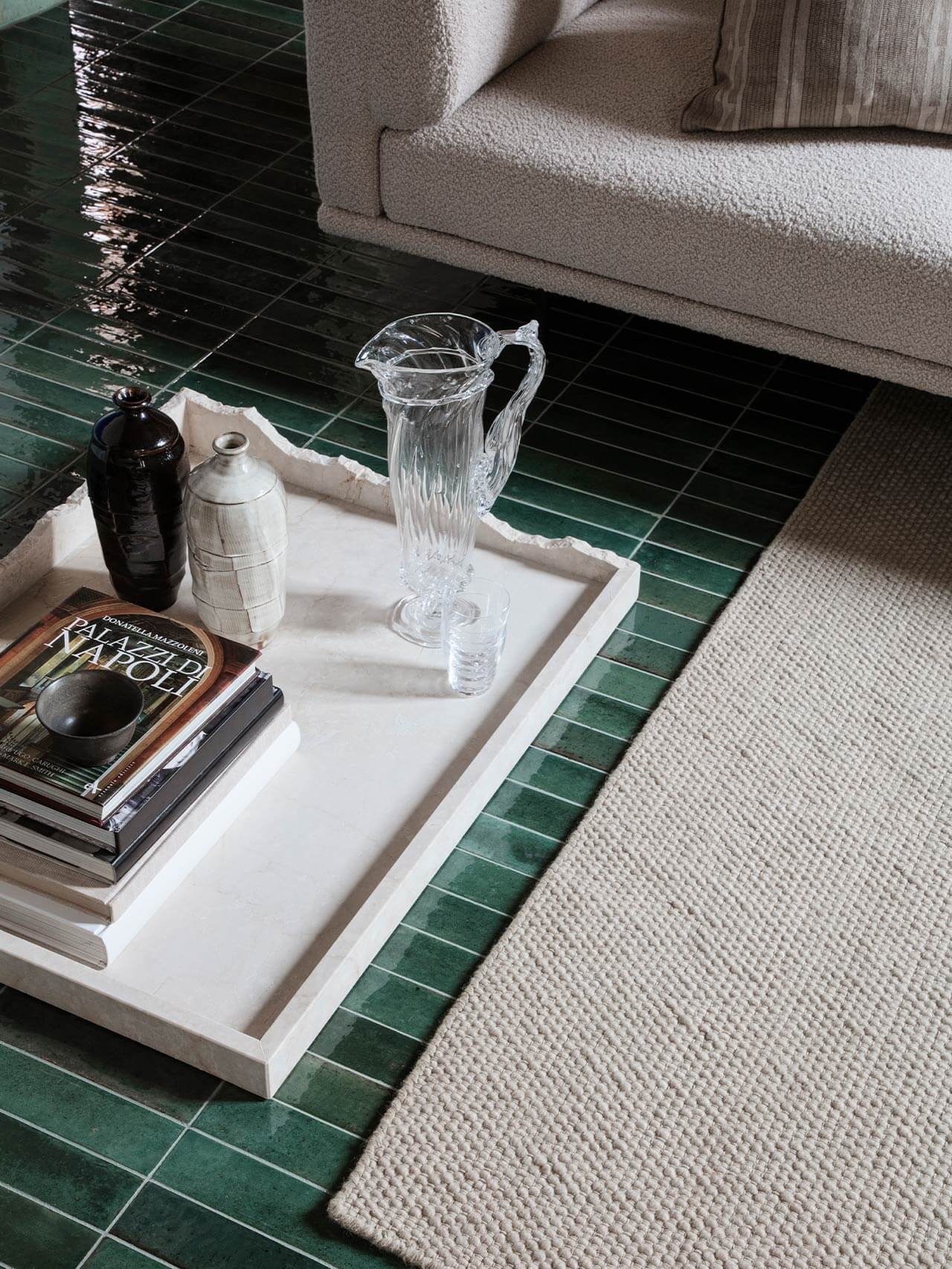 Vipp Palazzo Monti, Italy — Minimalist white marble tray on forest-green tile floor beside cream linen sofa, styled with clear glass pitcher, ceramic vessels, and art books.