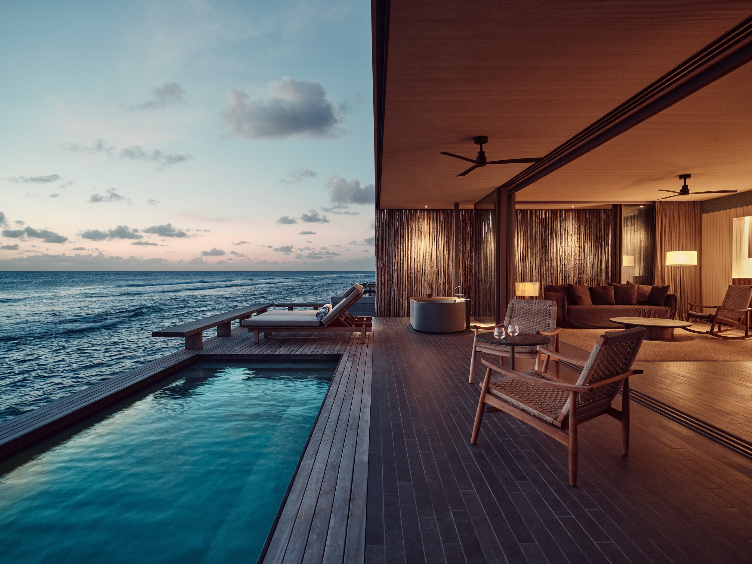 Patina Maldives, Asia — Overwater villa at sunset with infinity pool, teak deck, open-air living spaces, and ocean horizon views.