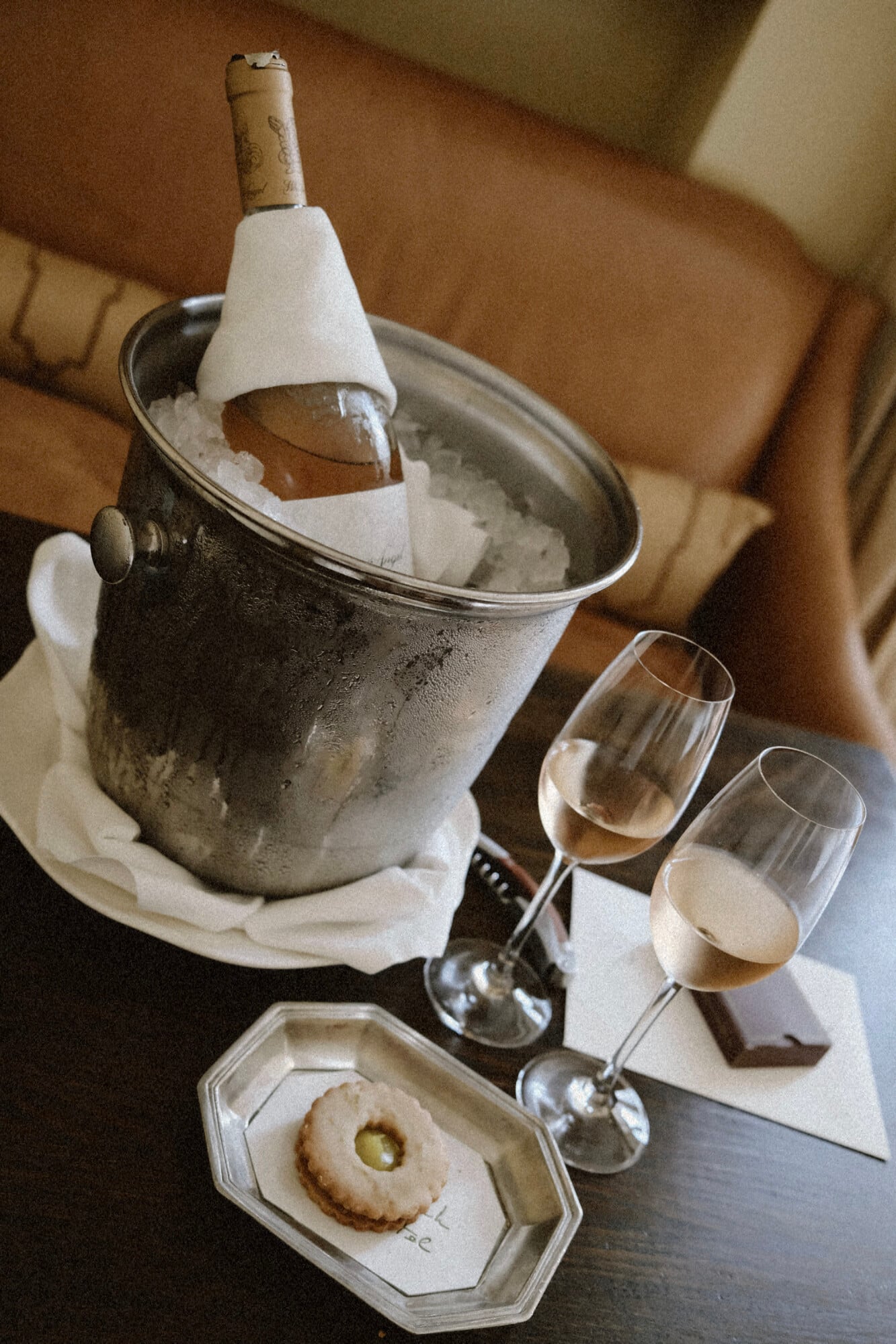 The Greenwich Hotel, New York, United States — Champagne bottle in frosted bucket with white napkin, wine glasses, and butter cookie on marble surface, warm interior lighting.