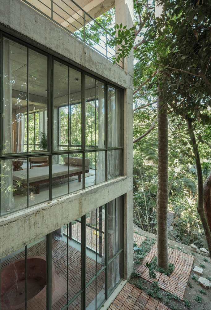 NICO, Mexico — Modernist concrete facade with steel-framed glass doors opening to forest canopy, multi-level wooden deck terracing through mature trees.