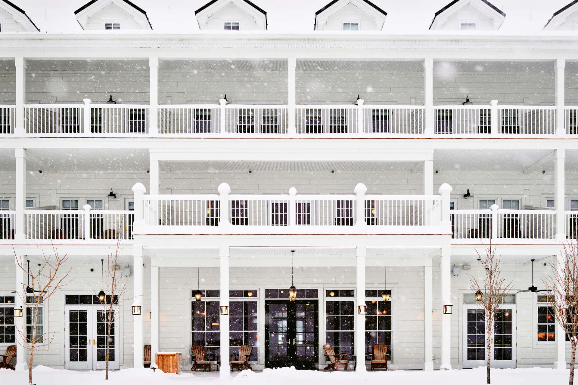 The Lake House, North America — Modernist waterfront hotel facade with white railings, arched windows, pendant lights, and snow-covered ground at dusk.