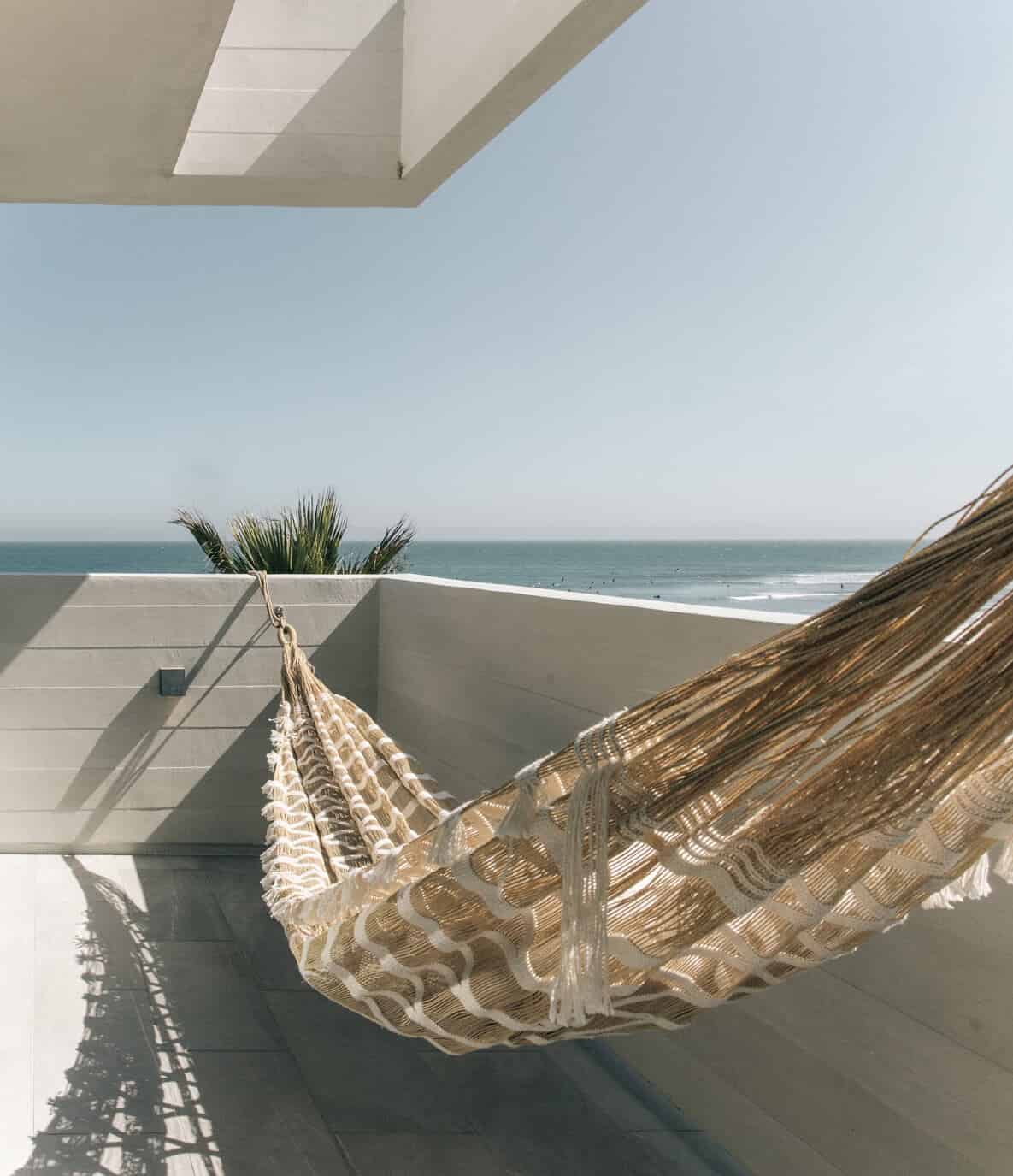 The Surfrider, North America — Coastal terrace with woven hammock, palm plant, and ocean view under modern concrete canopy.