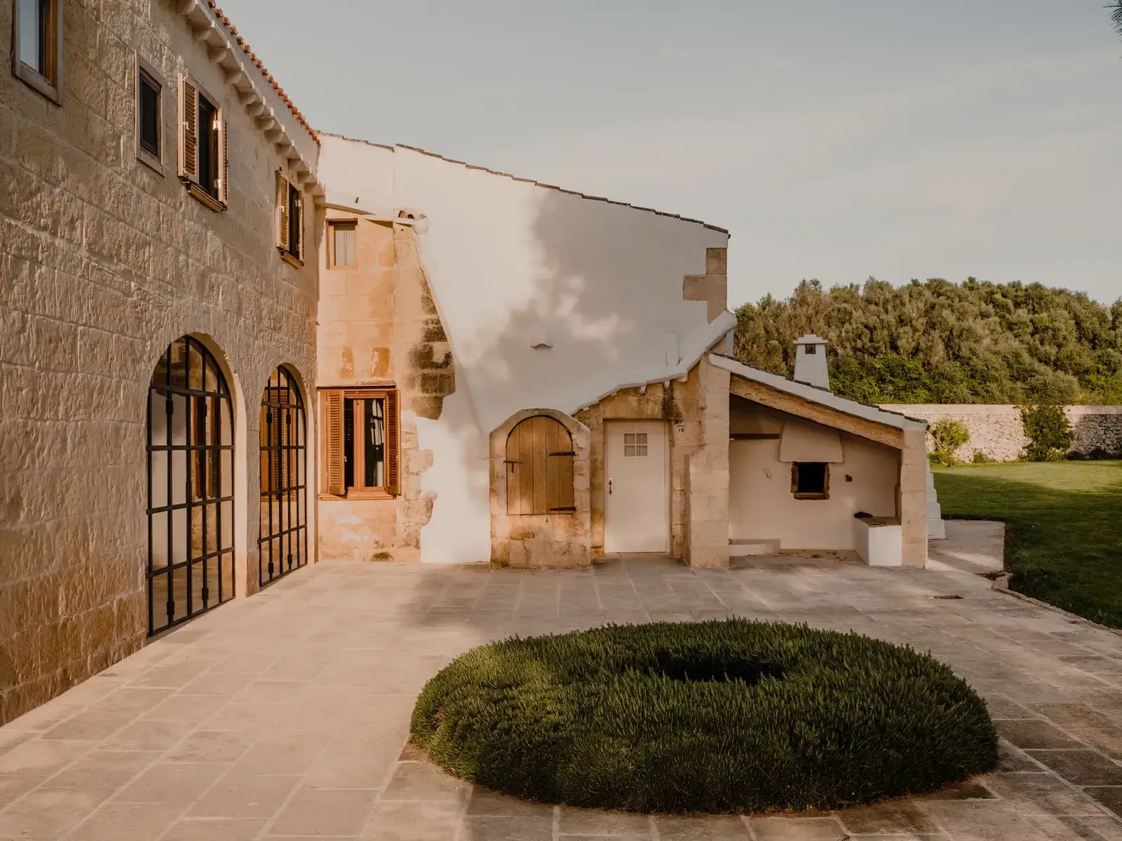Amagatay, Balearic Islands — Courtyard with stone buildings, arched doorways, terracotta tile paving, and manicured hedging in Mediterranean minimalist design.