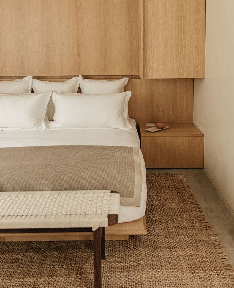 Octavia Casa, Mexico — Minimalist bedroom with walnut wood headboard, cream linens, natural fiber runner, and floating nightstand detail.