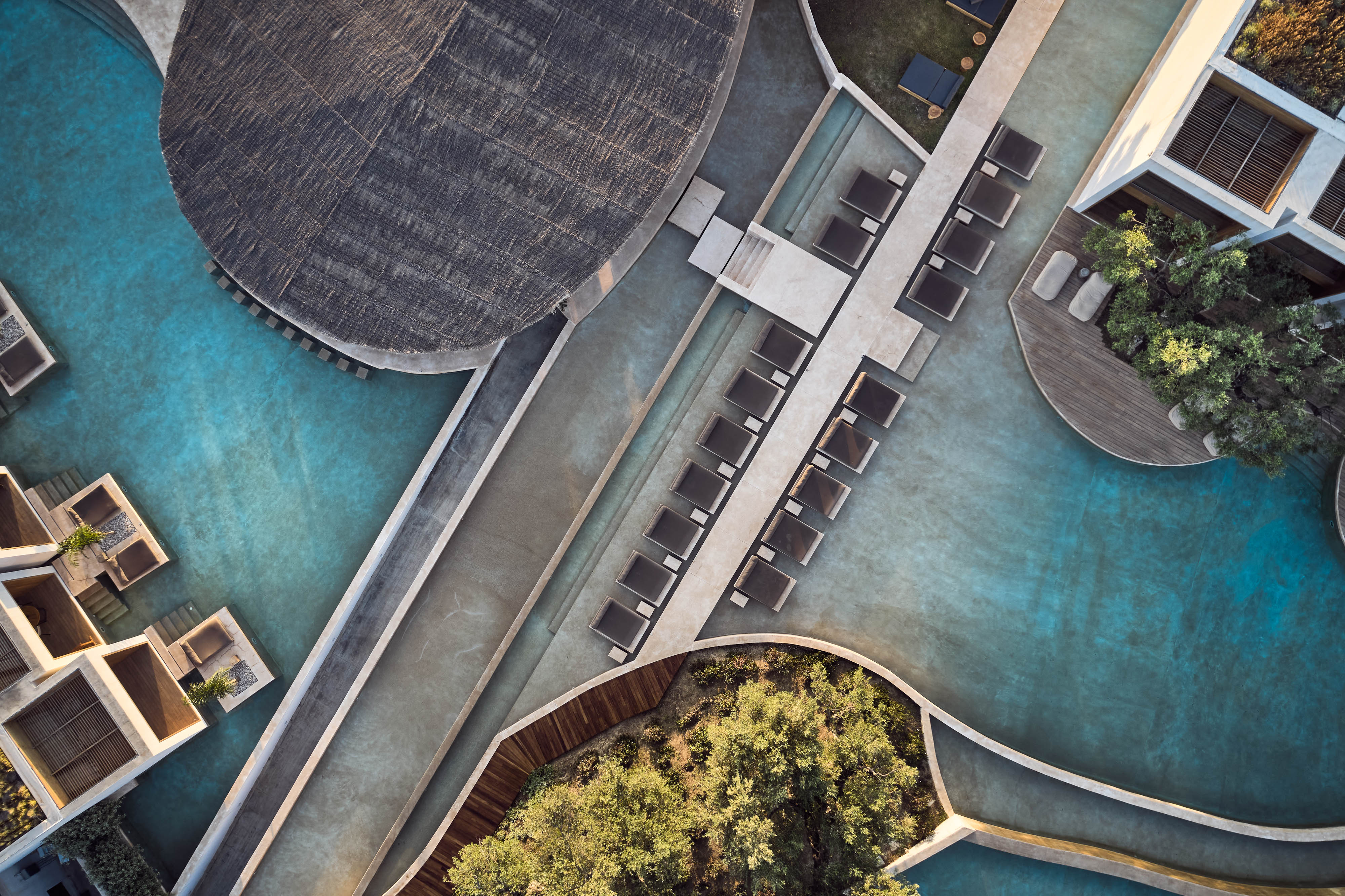 Aerial view of Olea All Suite Hotel's turquoise pools, dark loungers, and landscaped courtyards in geometric arrangement.