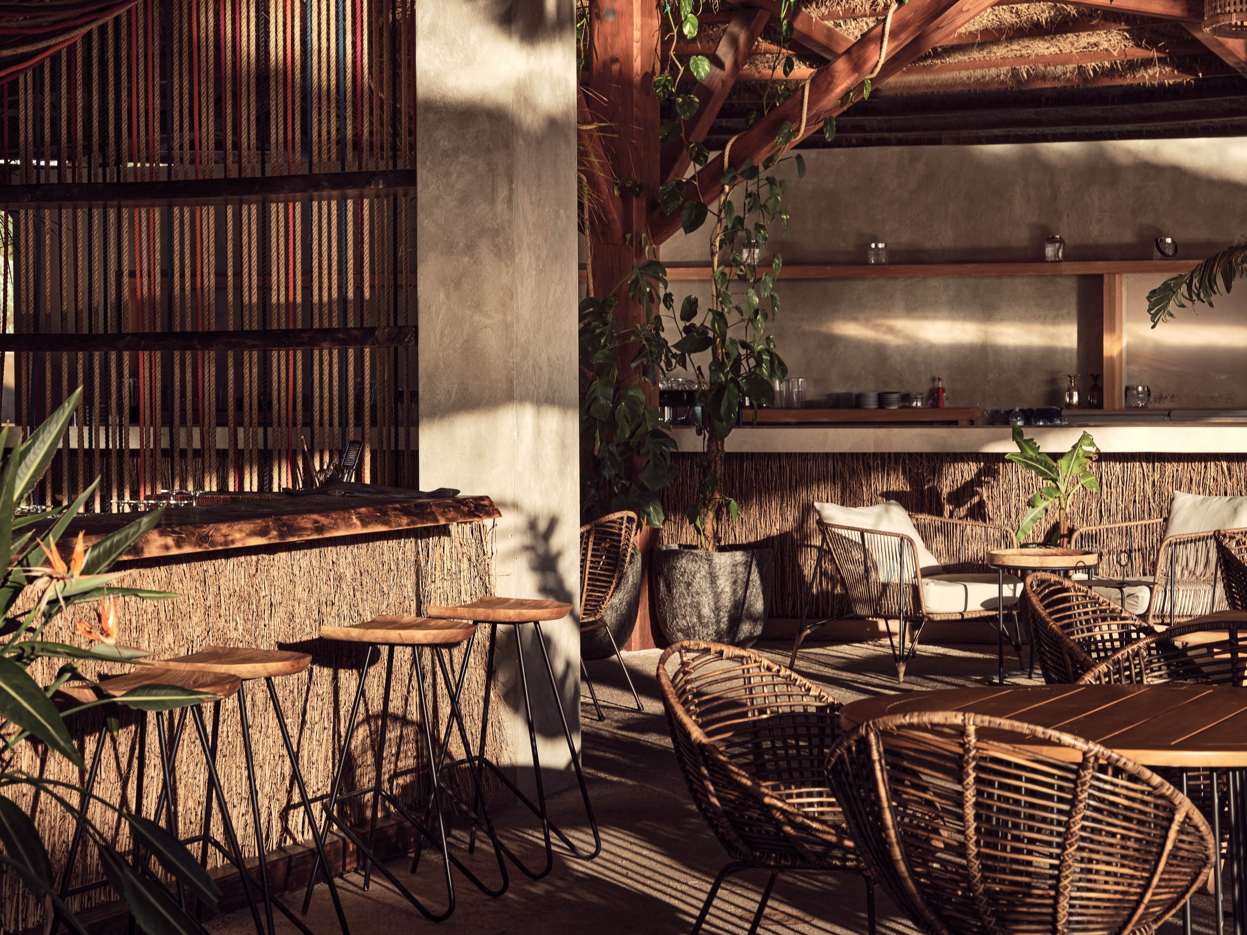 Olea All Suite Hotel, Europe — Rooftop lounge with woven chairs, wooden beams, concrete walls, and dappled sunlight casting geometric shadows across terrazzo flooring.