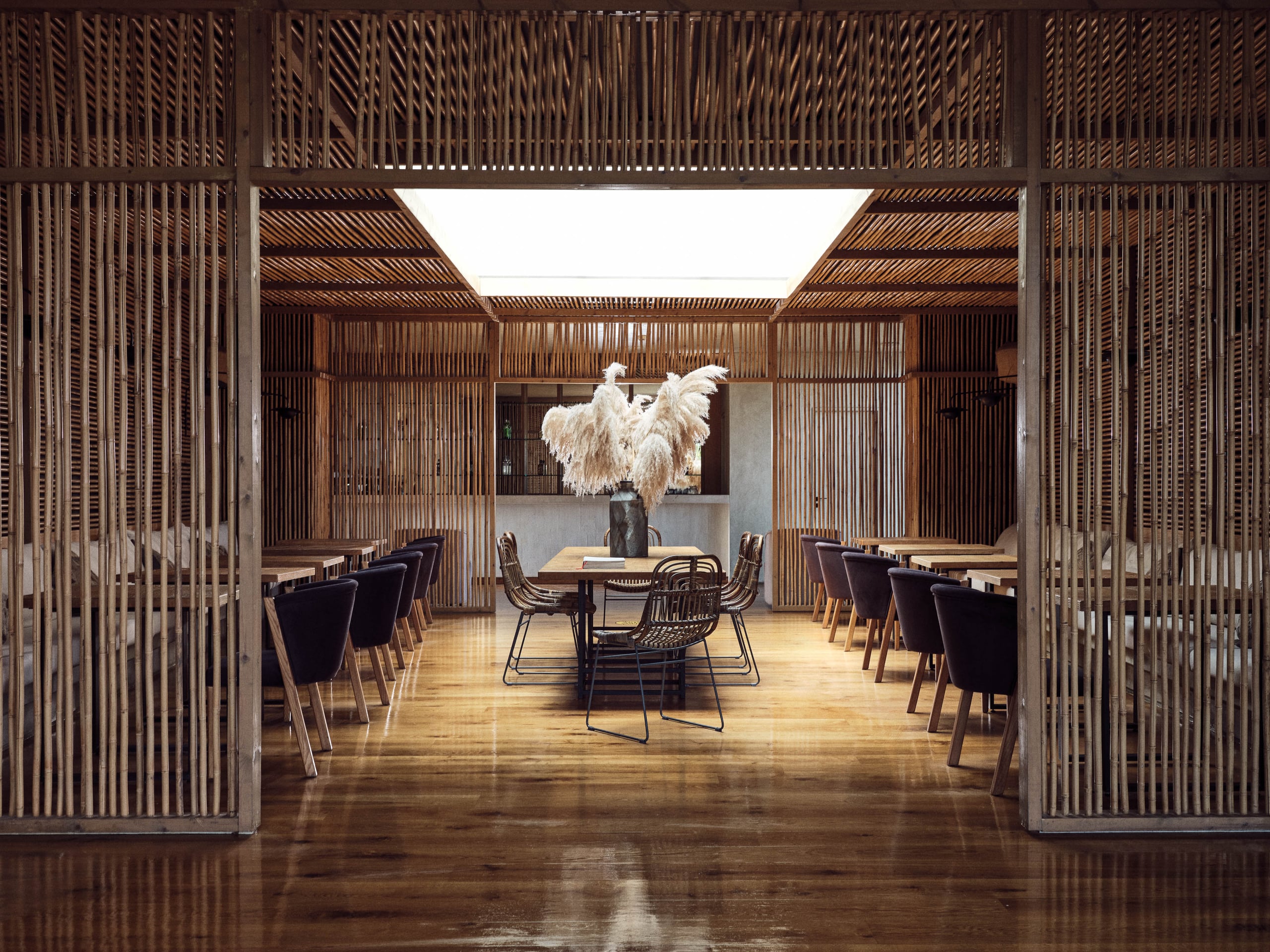 Olea All Suite Hotel, Europe — Minimalist dining pavilion with wooden slat screens, skylight, terrazzo floors, and pampas grass centerpiece.