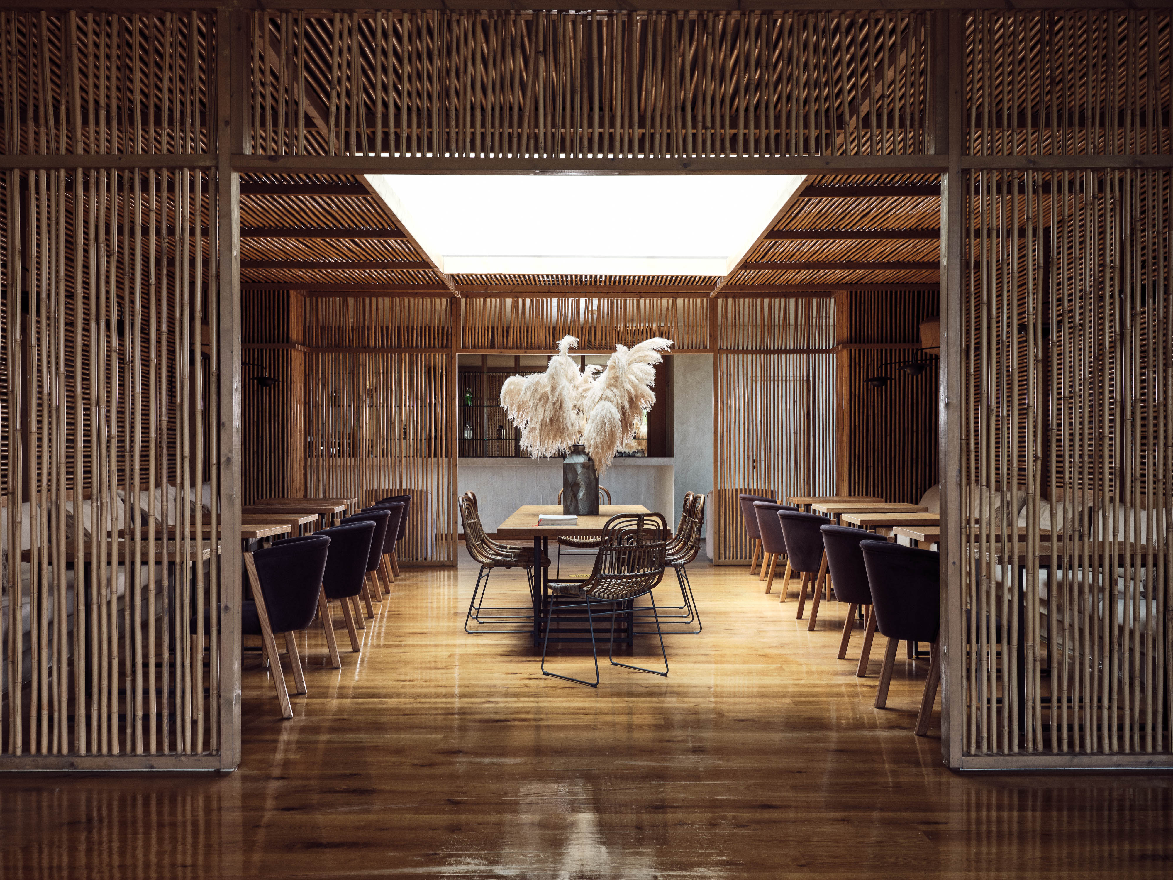 Olea All Suite Hotel, Europe — Minimalist dining pavilion with wooden slat screens, skylight, terrazzo floors, and pampas grass centerpiece.