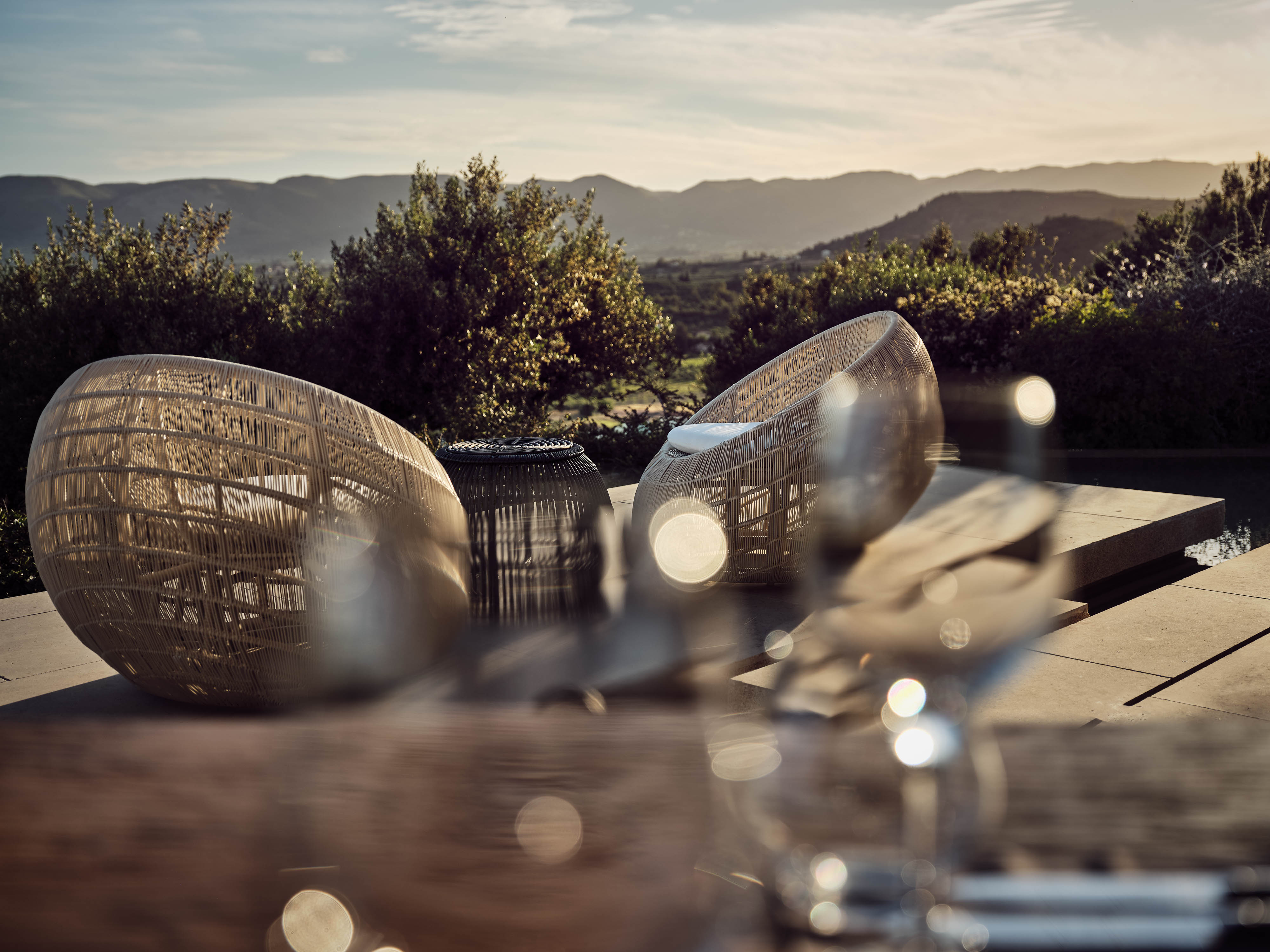 Olea All Suite Hotel, Europe — Woven rattan lounge chairs on terrace with olive grove views and mountains at golden hour.