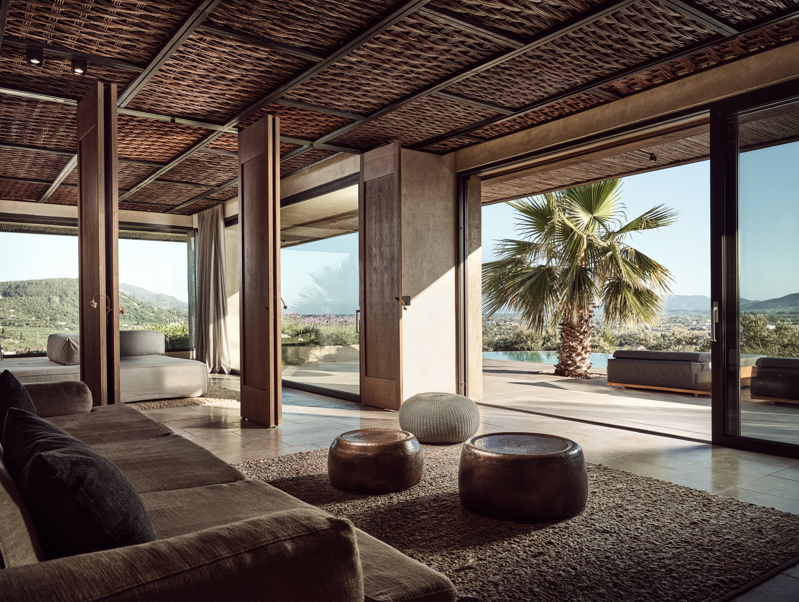 Olea All Suite Hotel, Europe — Open-plan lounge with woven ceiling, dark wood columns, contemporary furnishings, mountain and pool views.
