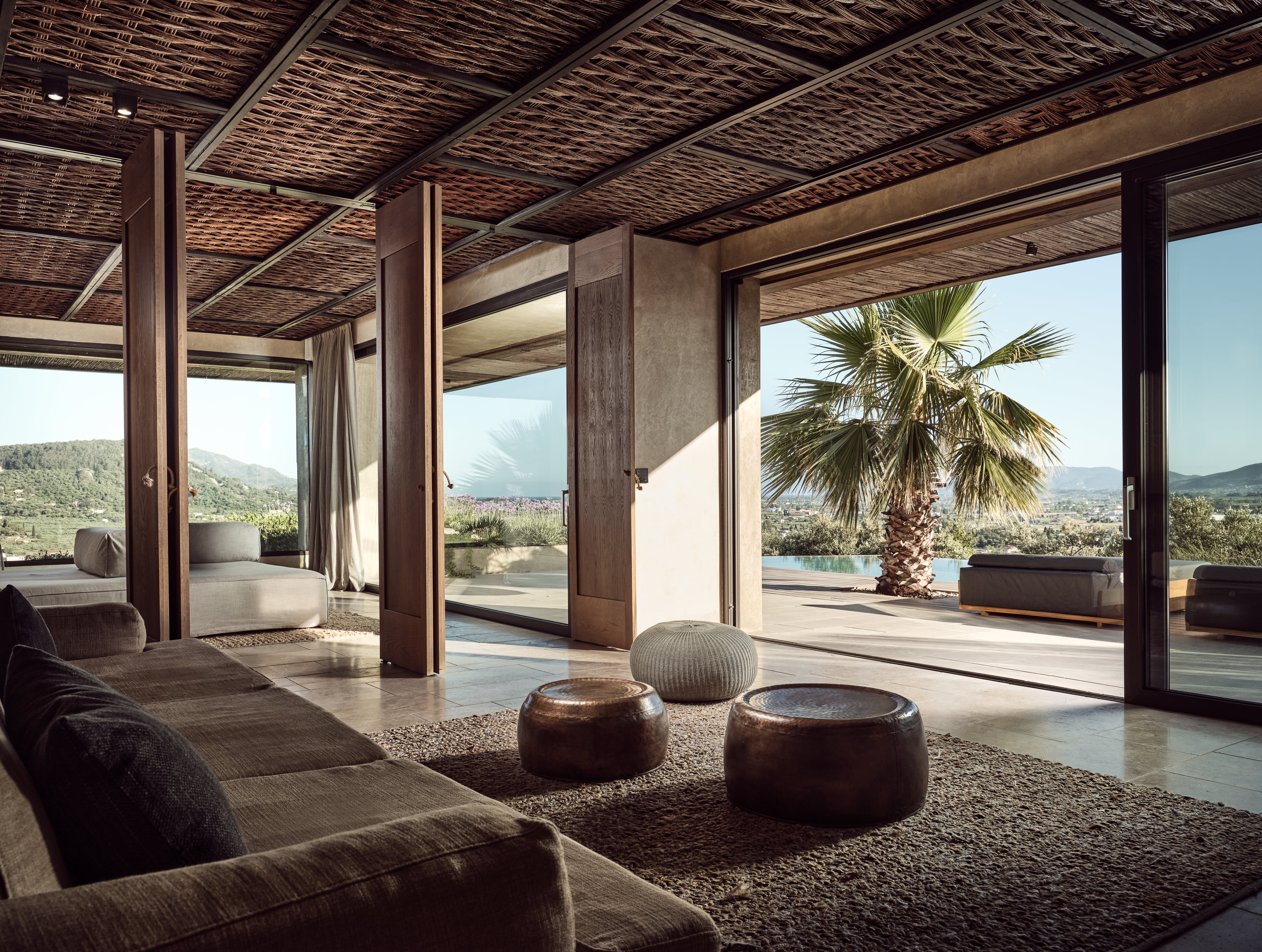 Olea All Suite Hotel, Europe — Open-plan lounge with woven ceiling, dark wood columns, contemporary furnishings, mountain and pool views.
