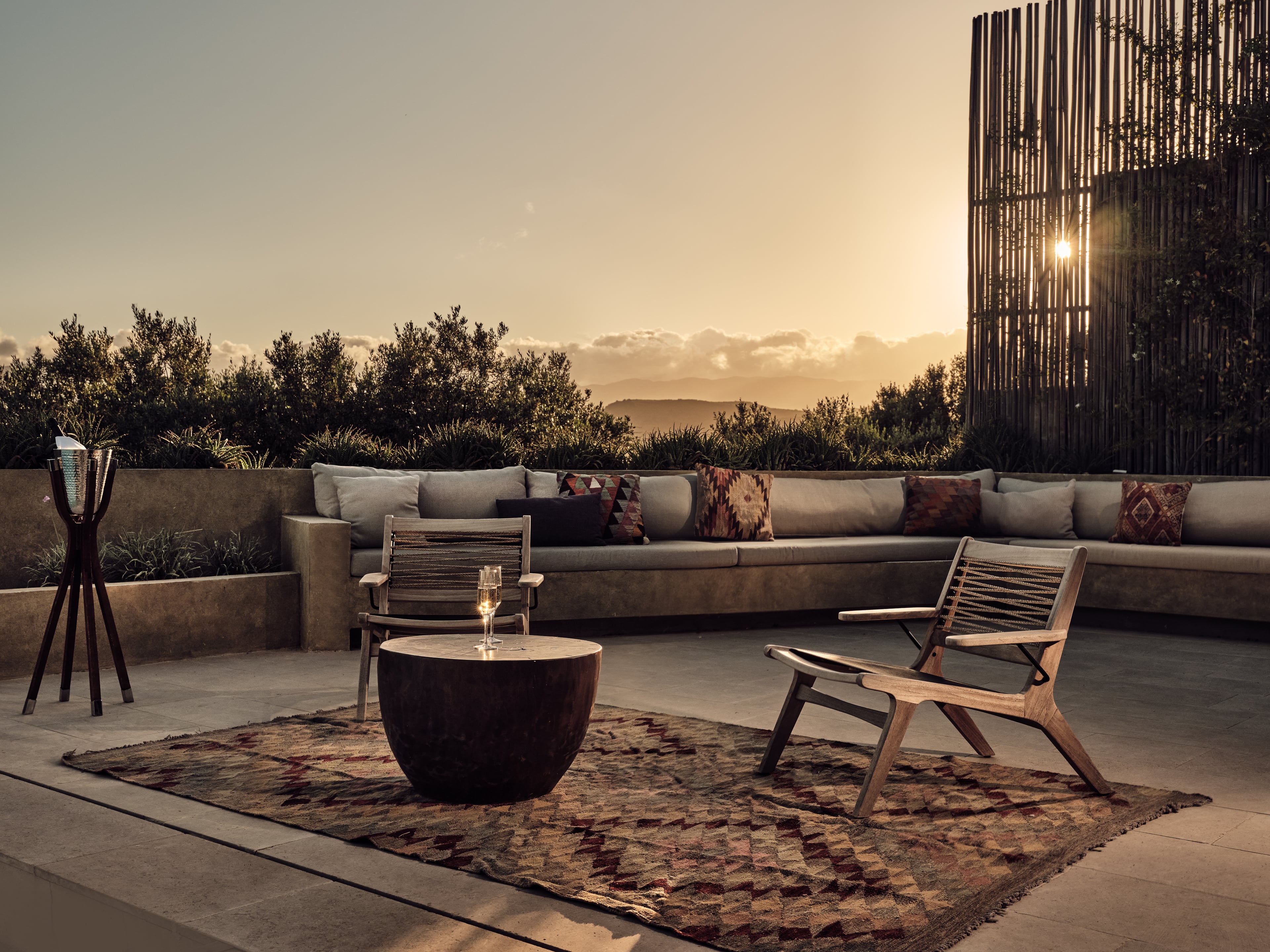 Sunset terrace at Olea All Suite Hotel with stone seating, wooden chairs, and mountain views framed by vertical timber screens.