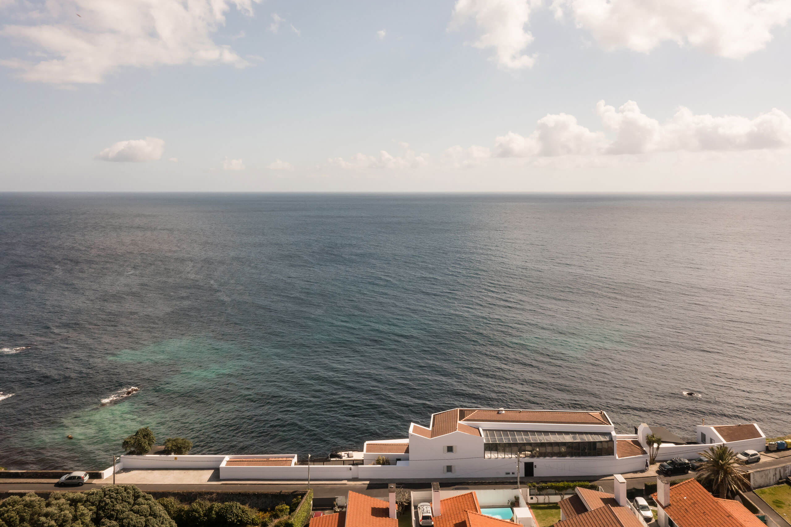 White Hotel, Europe — Modernist coastal resort with terracotta-roofed pavilions overlooking calm Mediterranean waters under soft clouds.