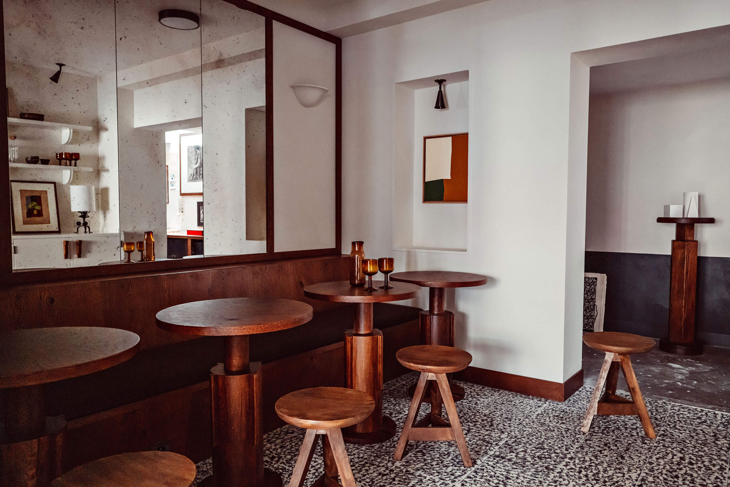 Académies et des Arts, Europe — Modernist lounge with cognac-toned wood furniture, terrazzo flooring, and travertine walls with mirror and artwork.