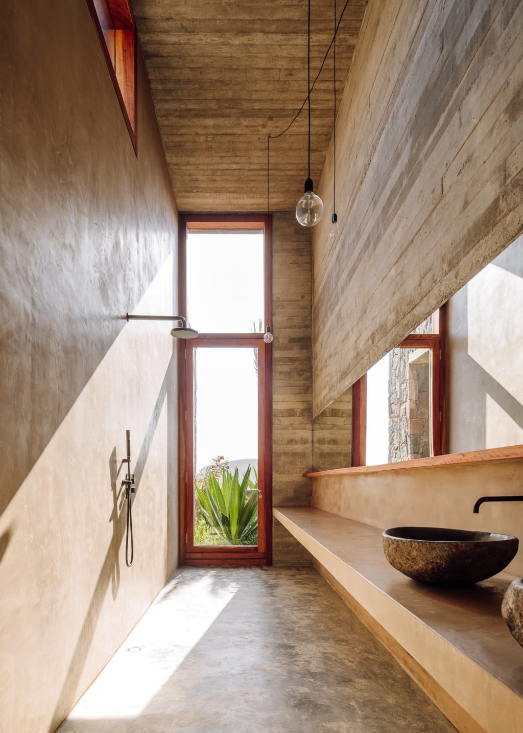 Barefoot Luxury, Africa — Minimal concrete bathroom with wooden ceiling, natural light through tall window, vessel sink, pendant fixtures, and open-air shower design.