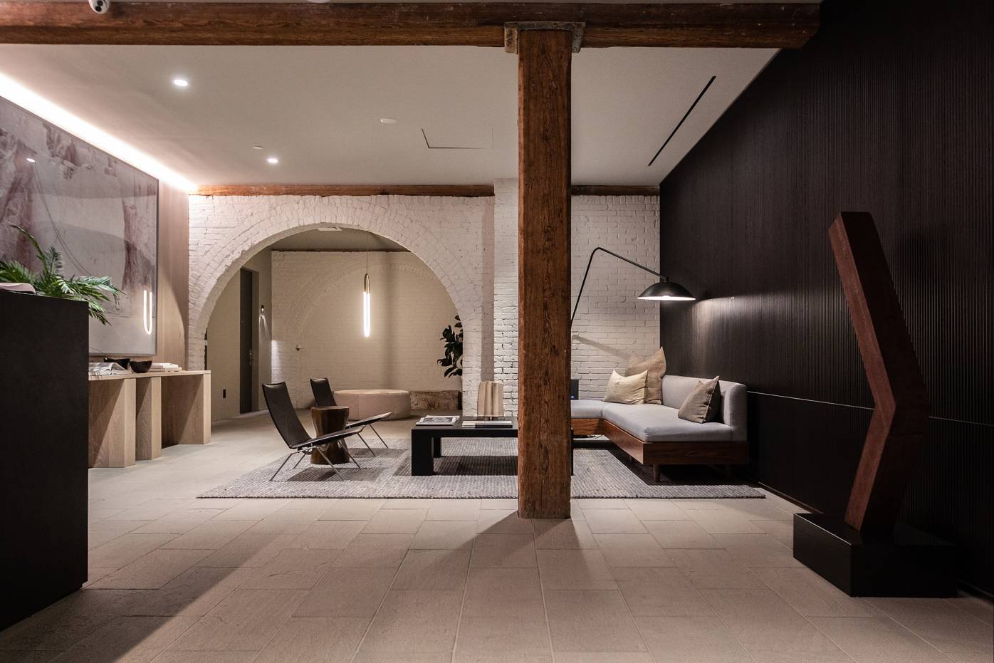 168 Plymouth, North America — Modern hospitality lobby with white brick archway, dark accent wall, wooden beam, concrete floors, and contemporary furniture under warm lighting.