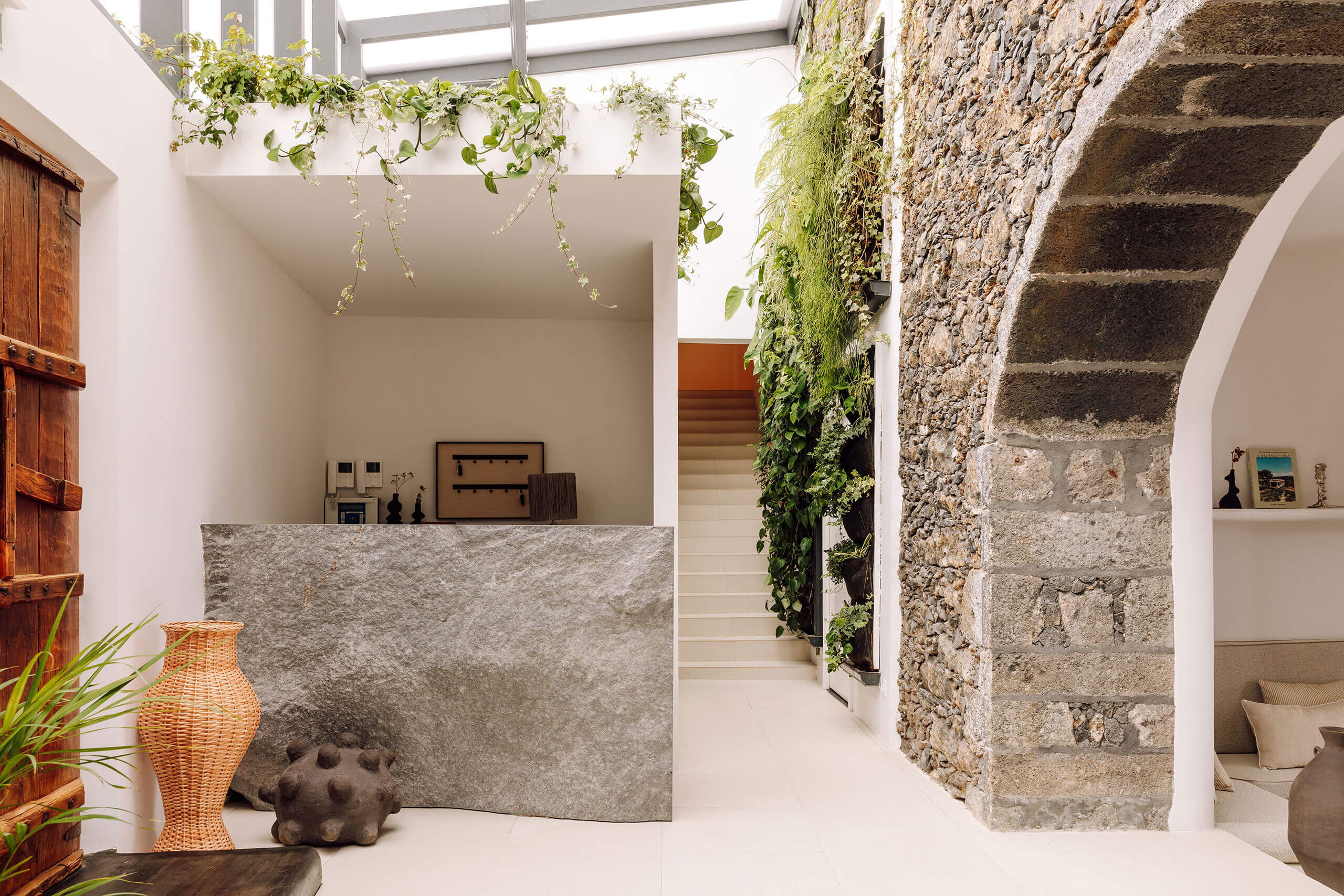 White Hotel, Europe — Minimalist entryway with limestone walls, climbing ivy, skylights, woven basket, and stone stairs leading upward in neutral palette.