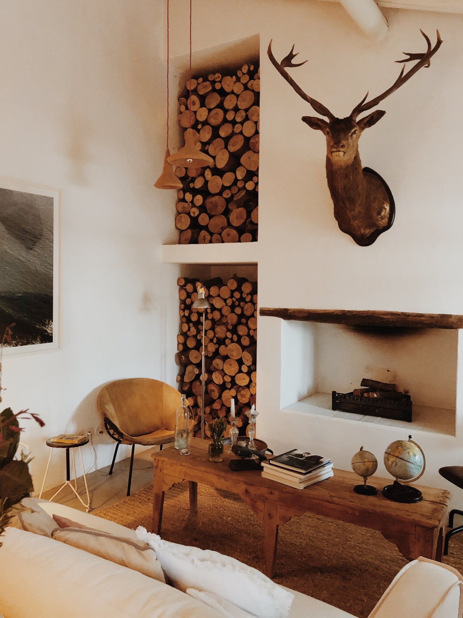 Pensão Agrícola, Europe — Modernist study with taxidermied deer head, stacked-wood wall installation, leather chair, wooden desk, and fireplace nook.