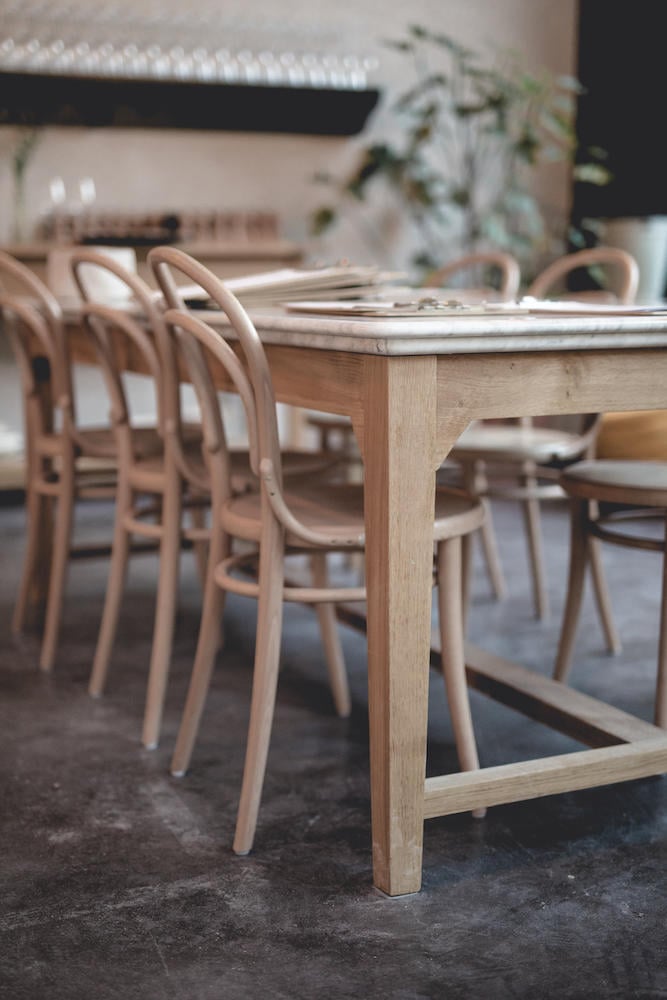 Le Barn, Europe — Light wood dining table with curved bentwood chairs on concrete floor, minimalist Scandinavian interior design with natural materials and soft daylight.