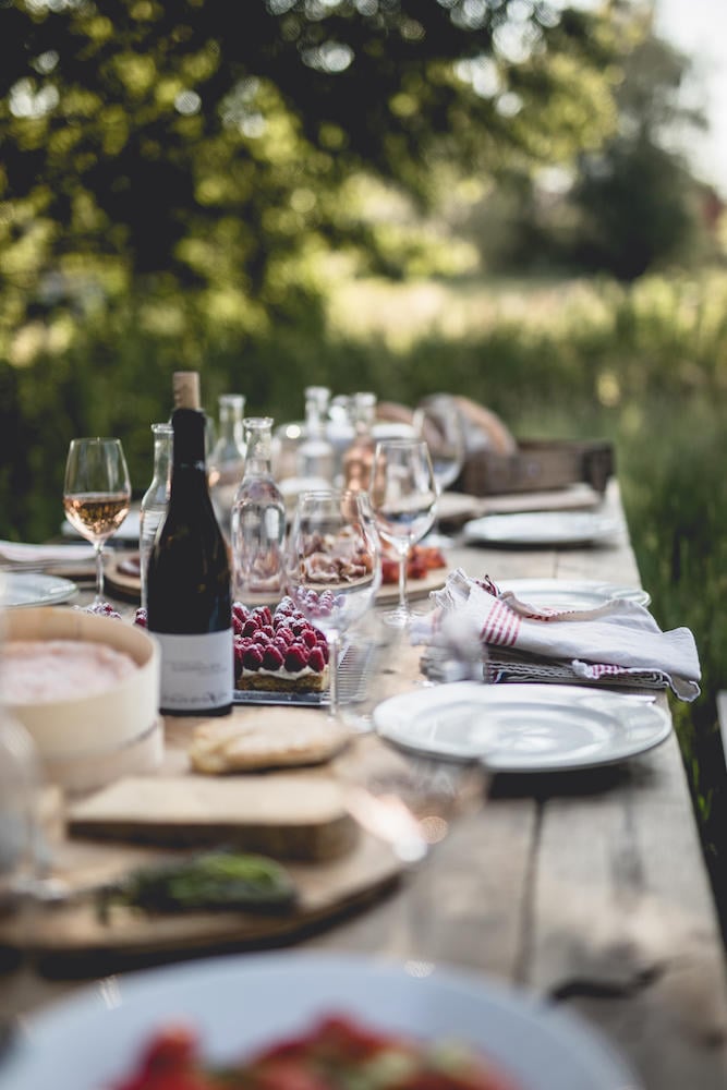 Le Barn, Europe — Outdoor dining table with wine glasses, place settings, and fresh berries under dappled garden light.