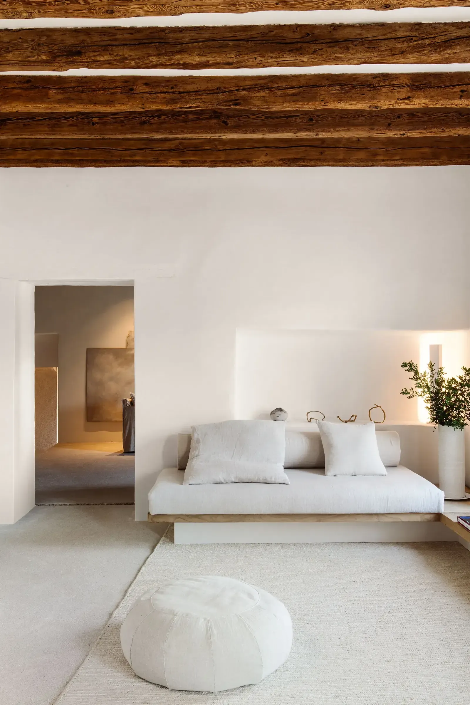 Es Racó d'Artà, Balearic Islands, Spain — Minimalist bedroom with exposed timber beams, white linen sofa, natural light, and earthy tones.