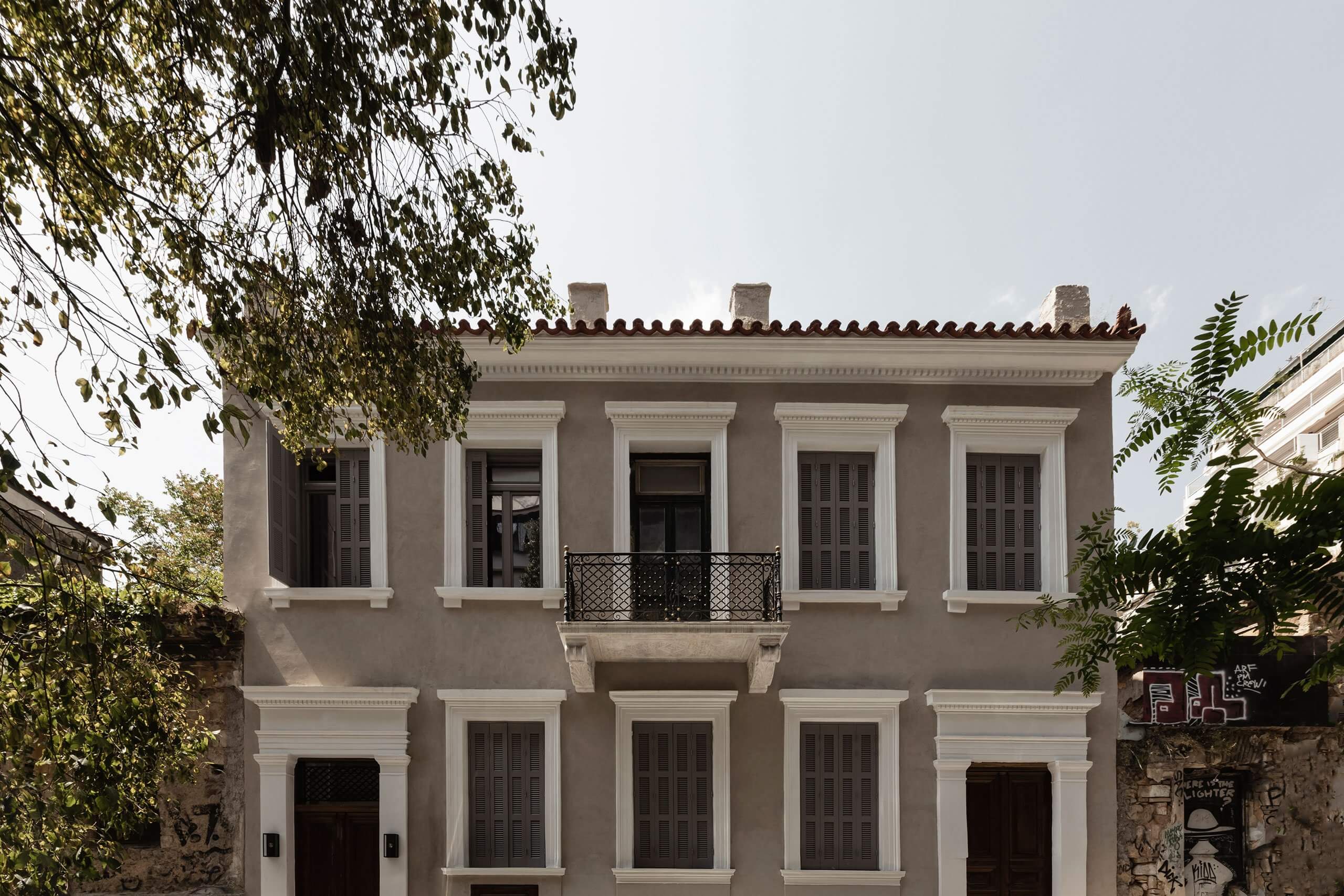 Casa Somos Suenos, Europe — Neoclassical facade with taupe stucco, white trim, black iron balcony, and tall shuttered windows framed by climbing vines.