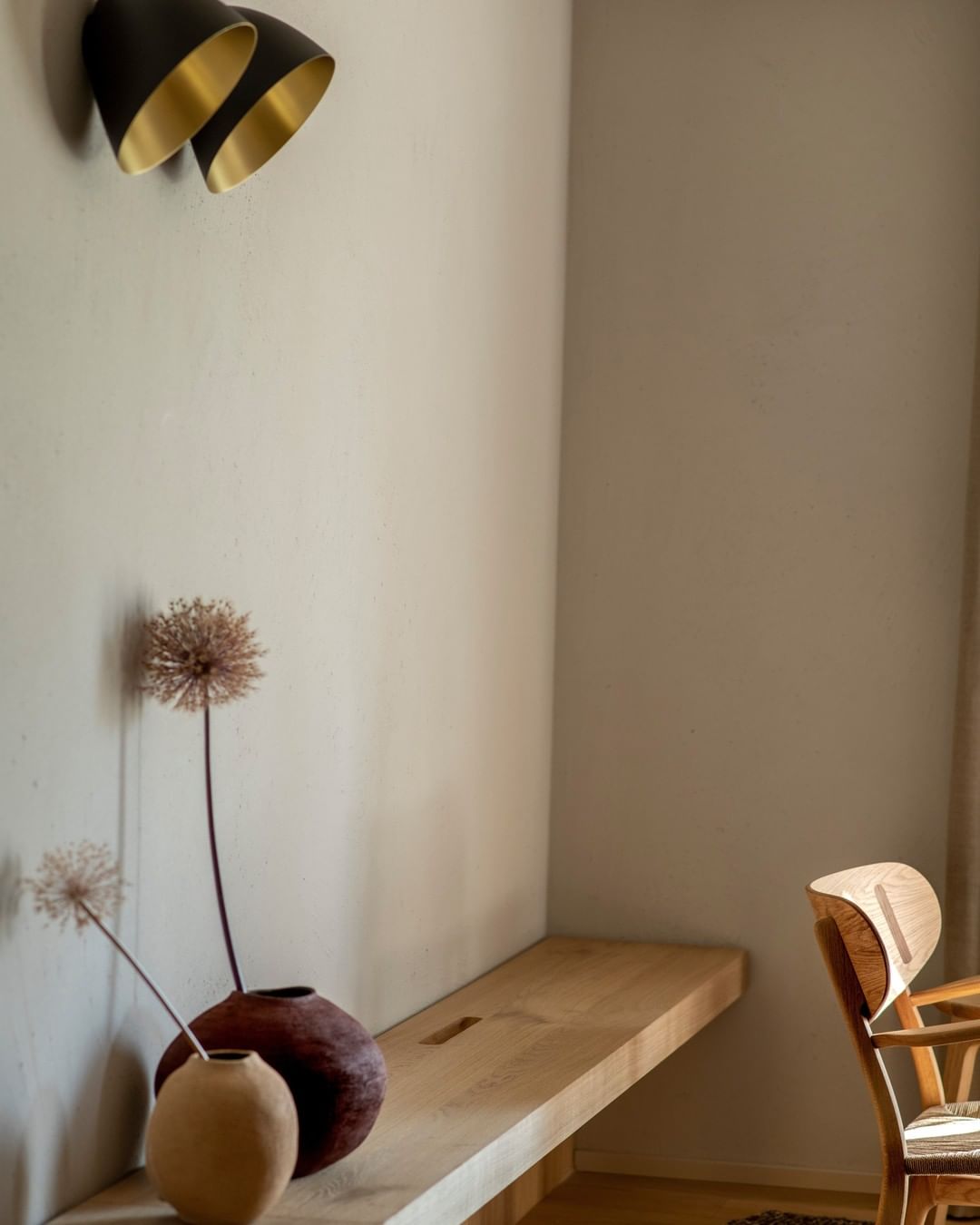 Casa di Langa, Europe — Minimalist corner with dried flowers in ceramic vessel, wooden desk, and brass wall sconces casting warm light on white plaster walls.