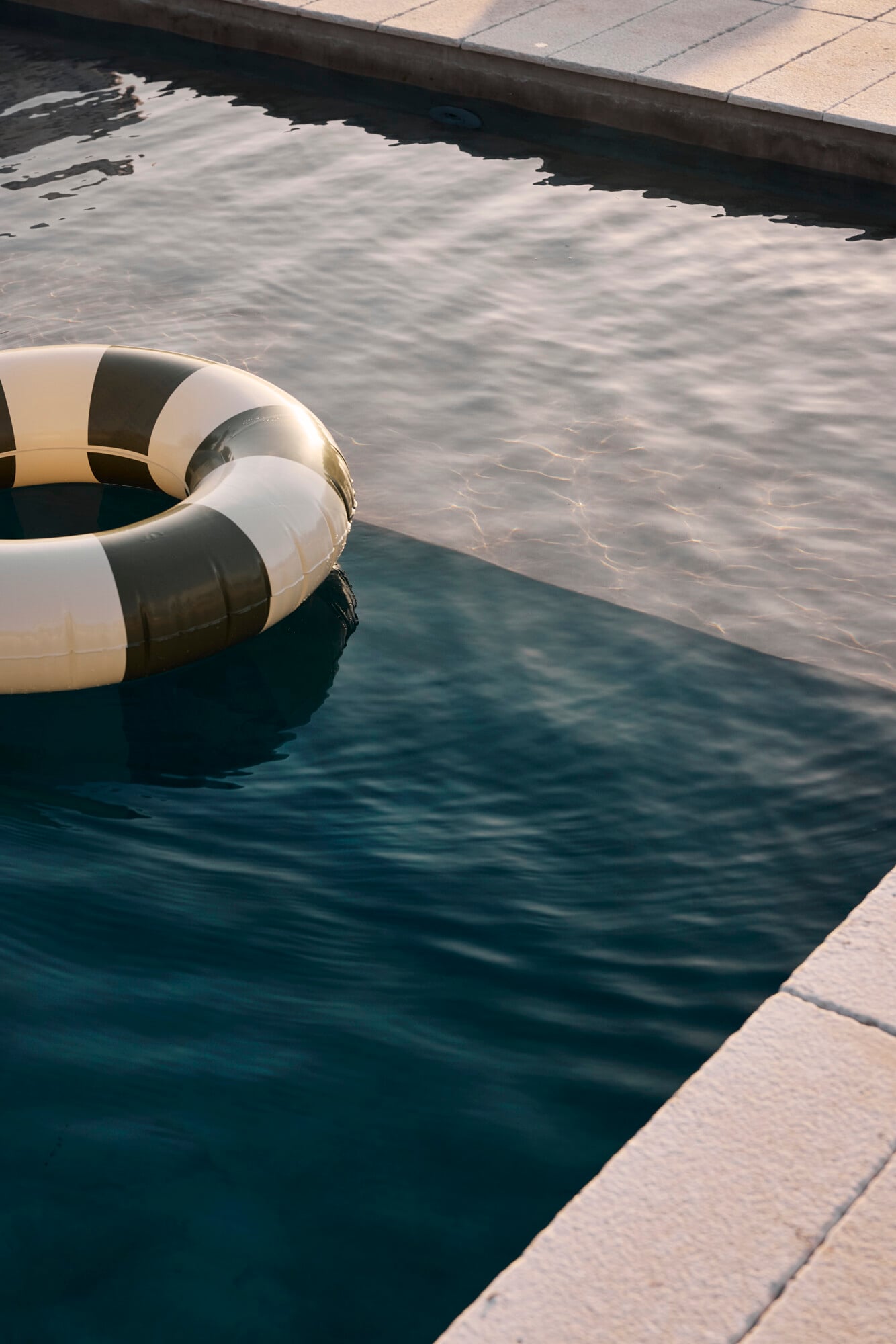 Villa Sessana, Italy — White and black striped life buoy floating in calm turquoise water beside stone dock, morning light reflecting off rippled surface.