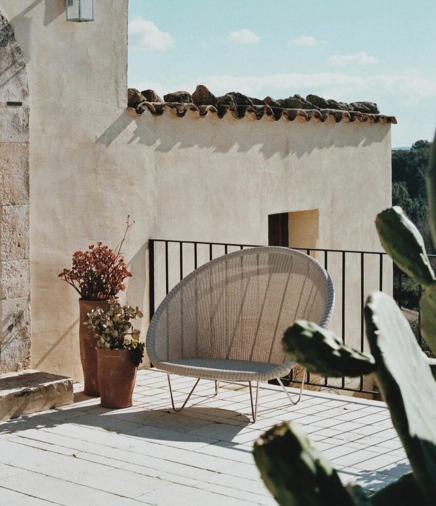 Dimora delle Balze, Europe — Whitewashed terrace with woven lounge chair, terracotta planters, black railing, and clay tile roof against Mediterranean landscape.